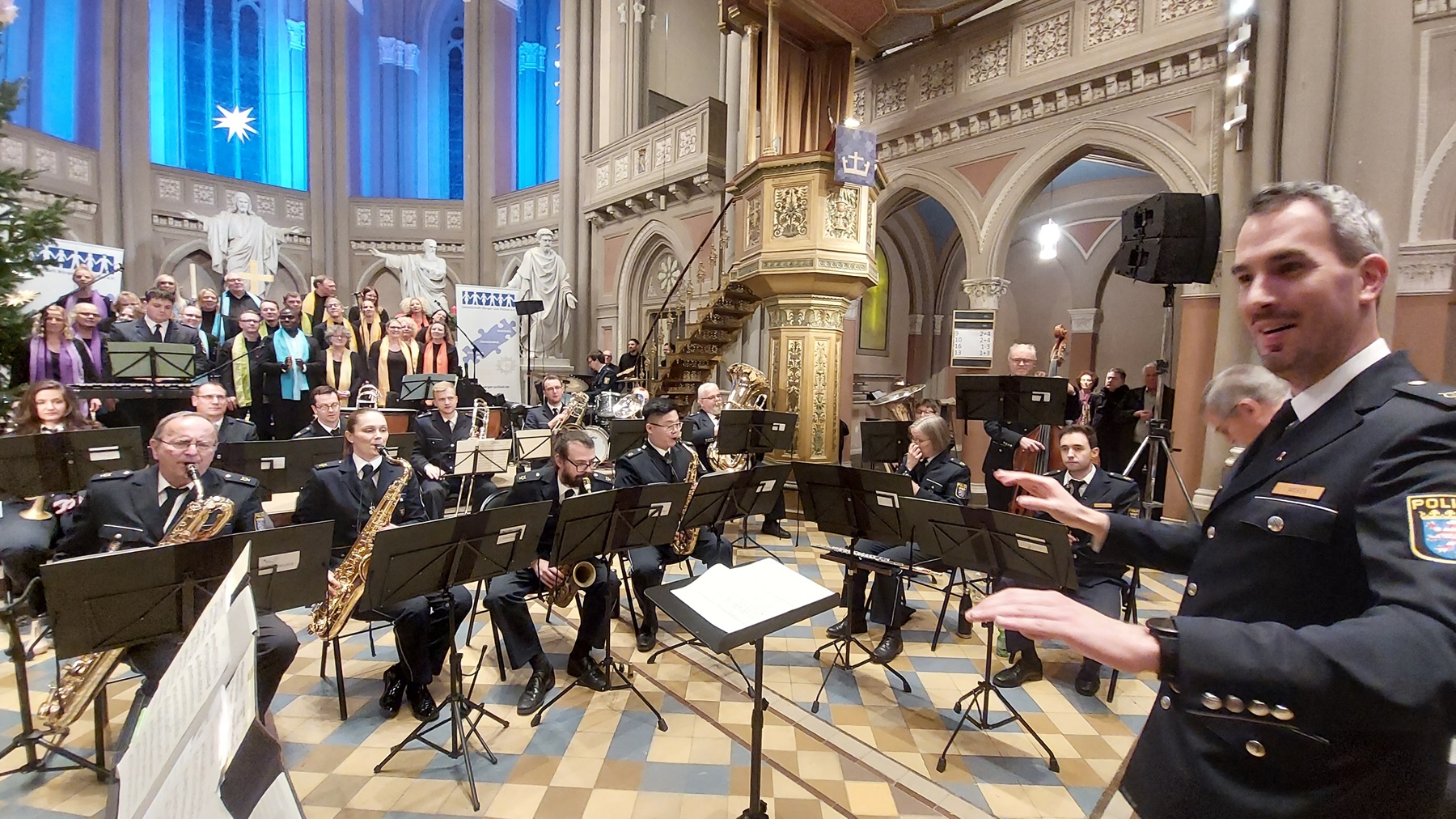 Im Altarraum sitzen die Musiker des Orchesters der Polizei. Alle tragen Uniform. Rechts im Vordergrund dirigiert Florian Weber.