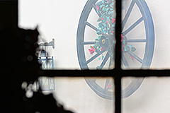 Blick auf ein Wagenrad an einer Wand durch ein Fenster im Gegenlicht