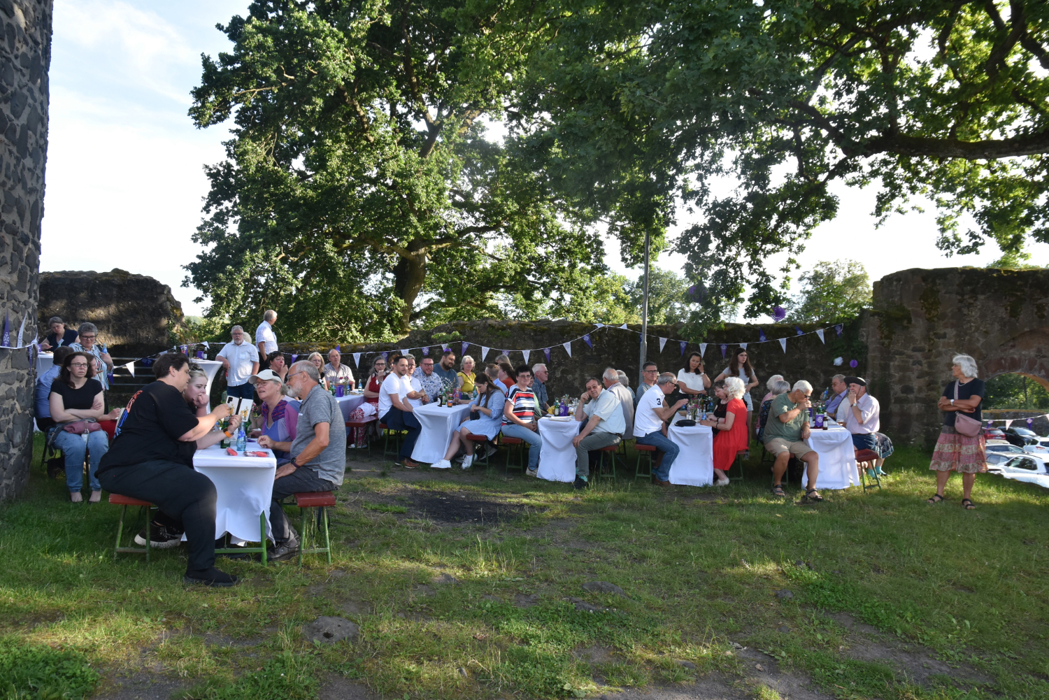Viele Festzeltgarnituren stehen auf einer Wiese neben dem Lißberger Burgturm. An den Tischen sitzen Menschen, essen und trinken. Ein großer Baum streckt seine Äste über das Geschehen.