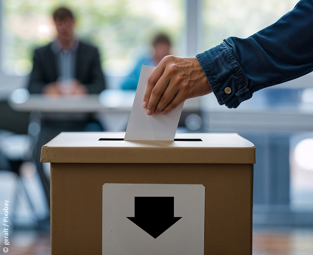 Hand wirft Stimmzettel in Wahlurne.