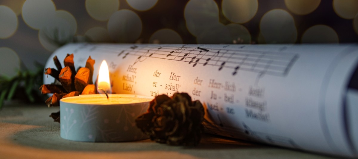 Brennendes Teelicht und Zapfen neben einem gerollten Notenblatt