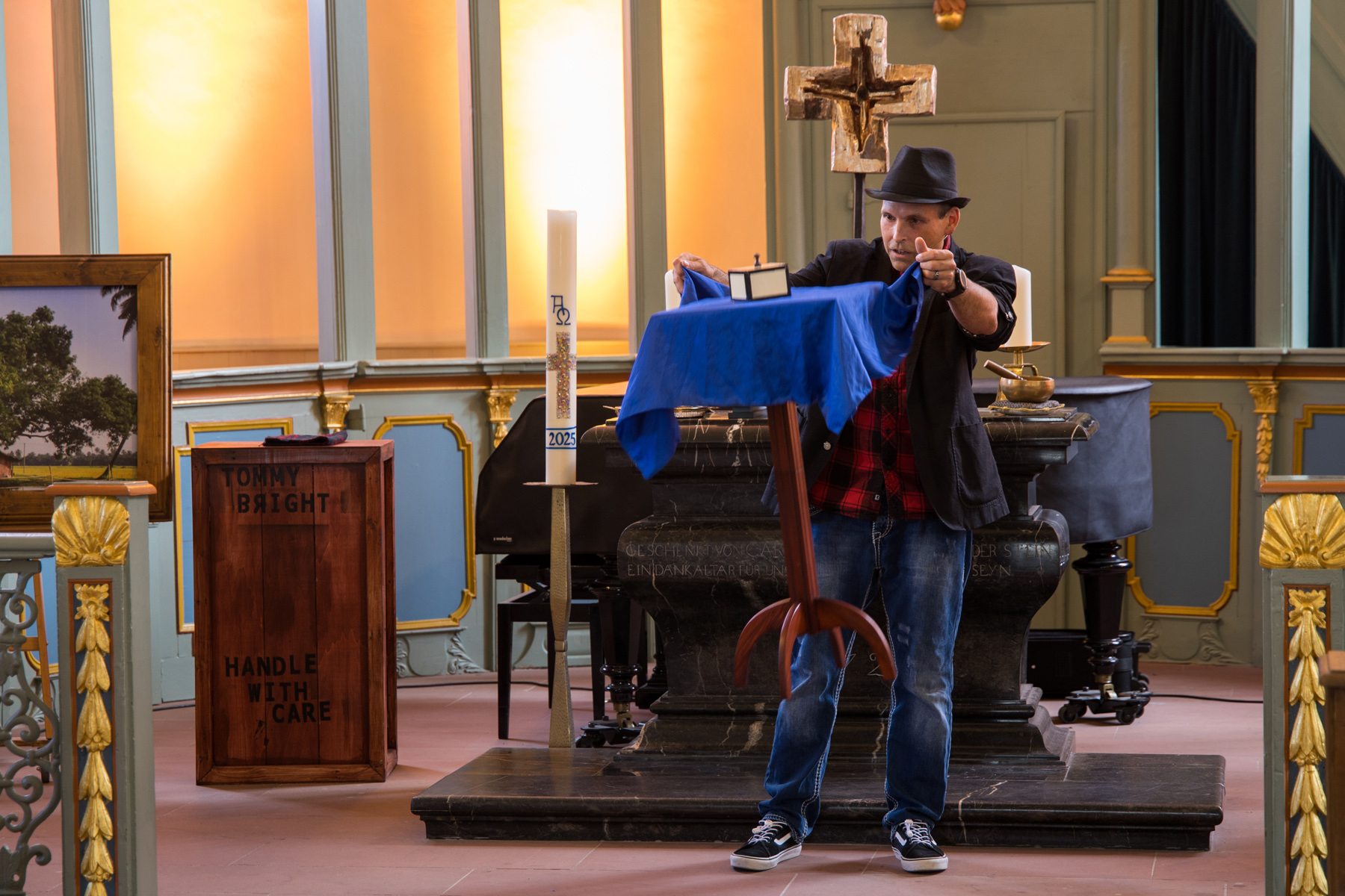 Illusionist Thommy Bright lässt einen Tisch schweben. Er steht mit Hut im Altaraum der Kirche und hat ein Blaues Tuch vor einem kleinen schwebenden Tisch in der Luft. 
