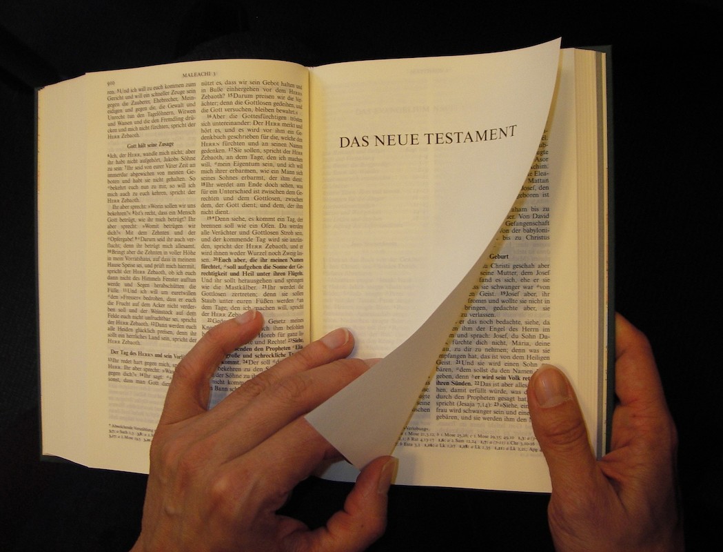 Hände blättern eine Seite der Bibel um