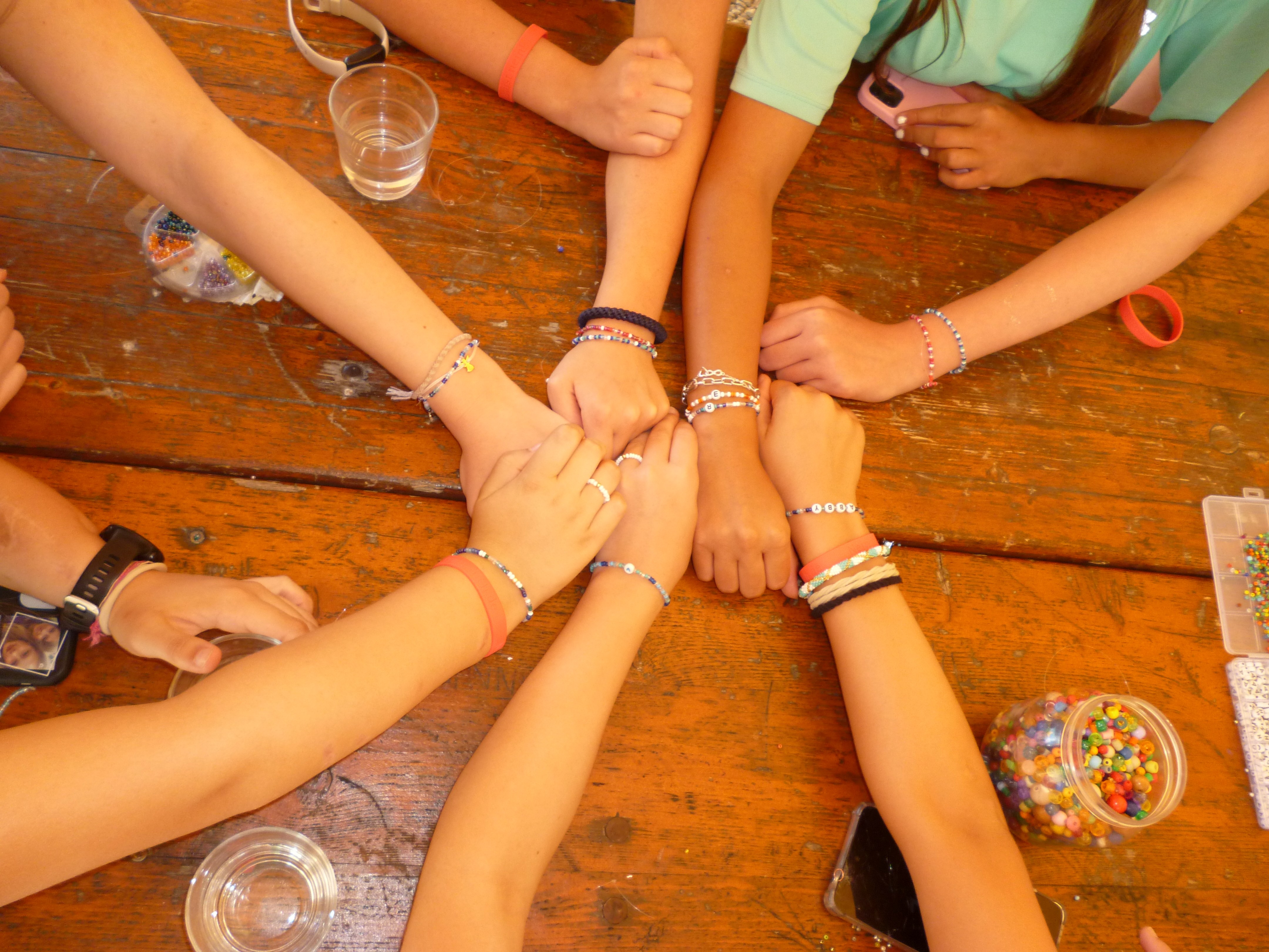 Hände von Jugendlichen treffen sich in der Mitte eines Tisches, sie tragen Freundschaftsarmbänder