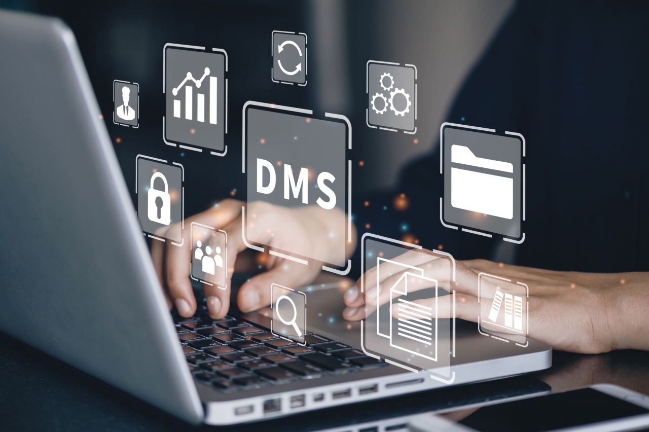 Person tippt auf einem Laptop, während digitale Symbole für Dokumentenmanagement (DMS) wie Ordner, Diagramme, Schloss und Zahnräder holografisch über der Tastatur schweben.