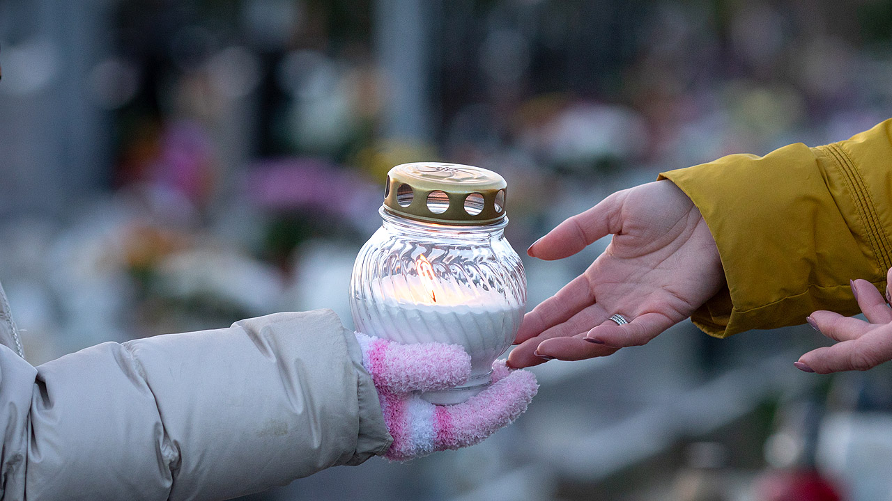 Ein Windlicht wird auf einem Friedhof von einer Hand in die andere weiter gegeben