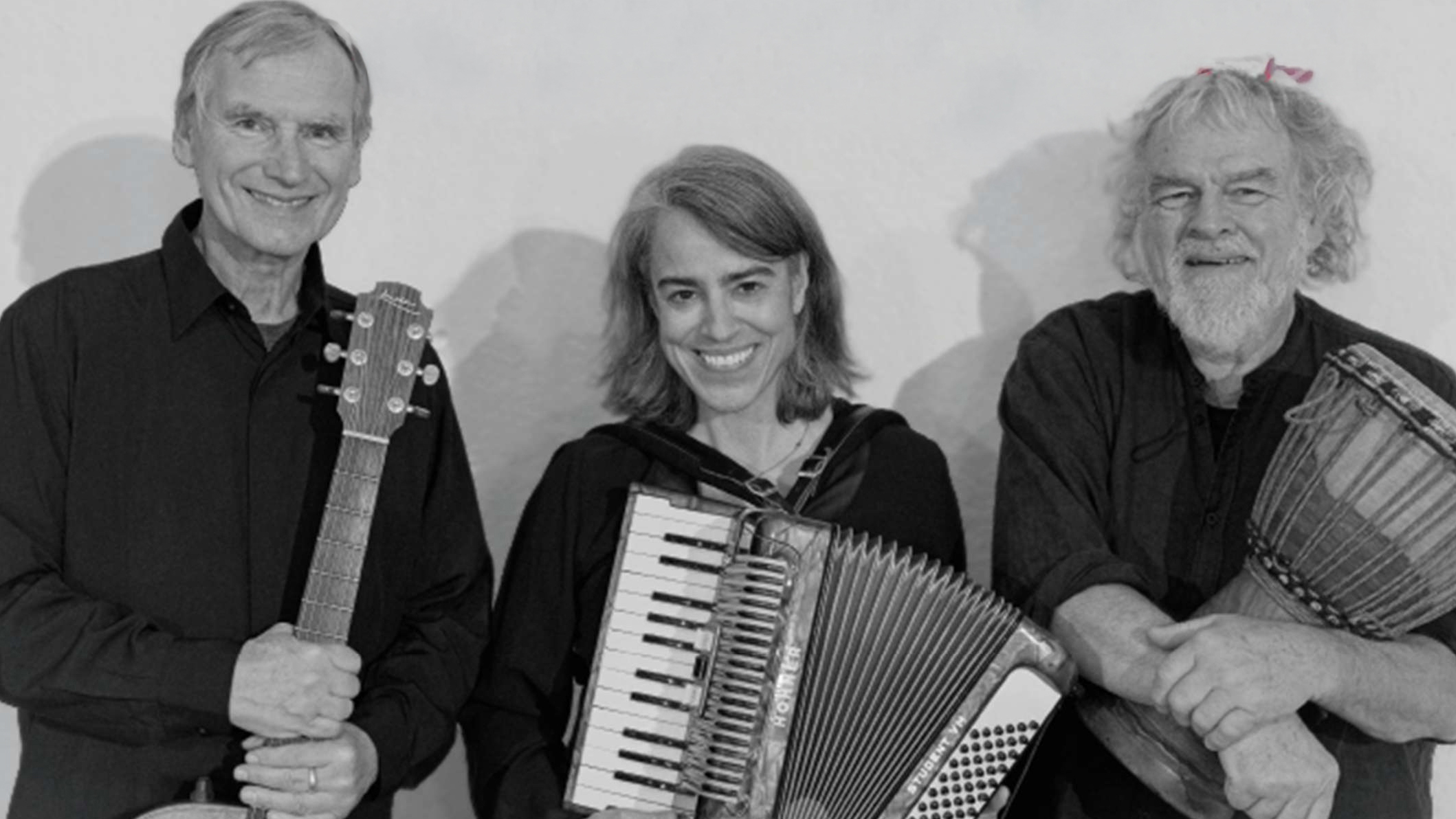 Drei lächelnde Personen mit Musikinstrumenten: links eine Gitarre, in der Mitte ein Akkordeon und rechts eine Trommel.