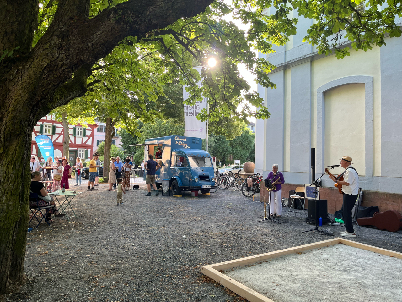 Livemusik, Foodtruck und Gäste unter Kastanienbäumen beim KulturGenuss an der Friedberger Burgkirche.
