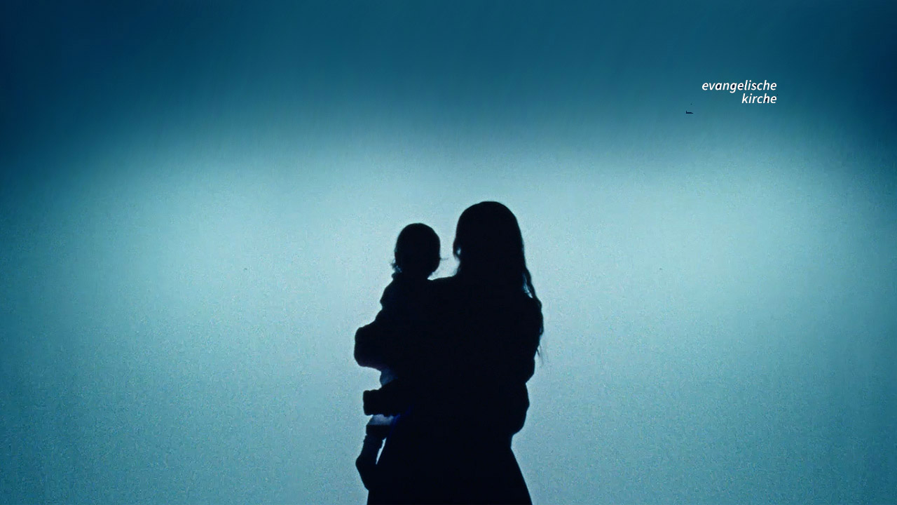 Silhouette einer Mutter mit Kind vor türkisfarbenem Lichtschein