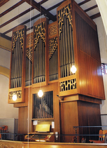 Große Kirchenorgel aus hellem Holz mit mehreren Pfeifenreihen und beleuchtetem Spieltisch im Innenraum einer Kirche.