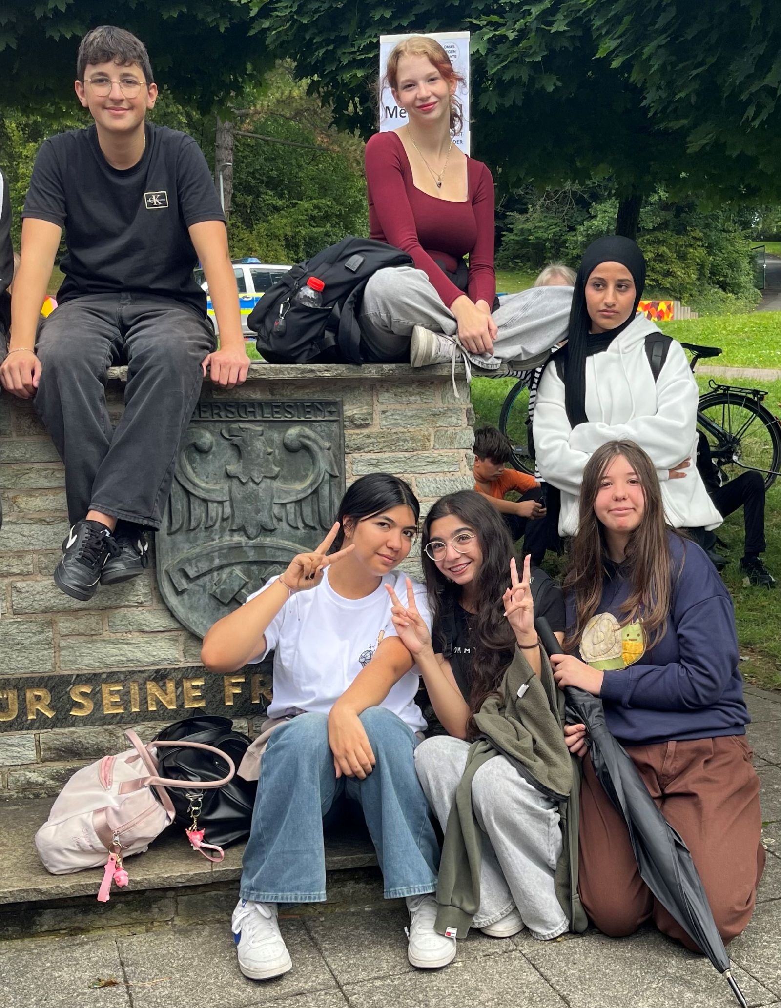 Bildung gegen rechts, Einsatz gegen Aschiebungen an Schulen Fünf Schülerinnen und ein Schüler sitzen draußen auf einer Mauer und machen das Peacezeichen, sie setzen sich gegen die Abschiebung ihrer Mitschüler ein