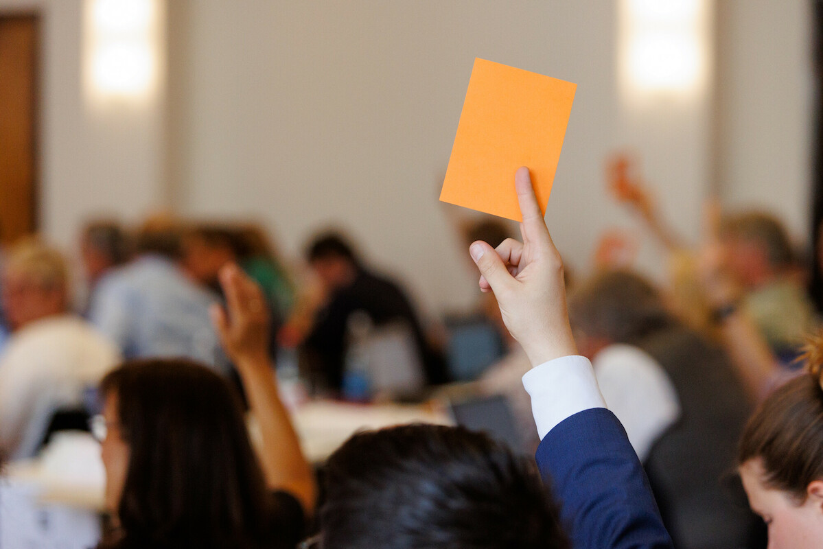 Man sieht auf Hände, die einen orangenen Abstimmzettel halten