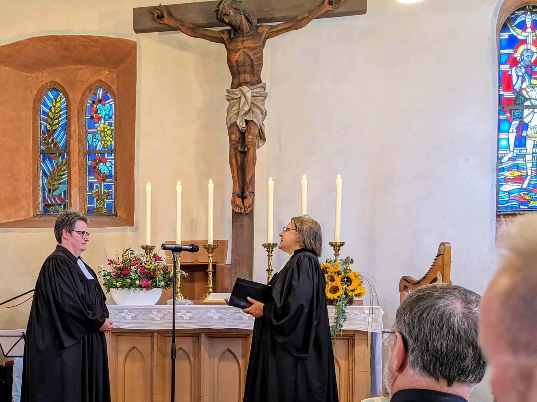 Zwei Frauen, beide im schwarzen Talar, stehen vor einem Altar.
