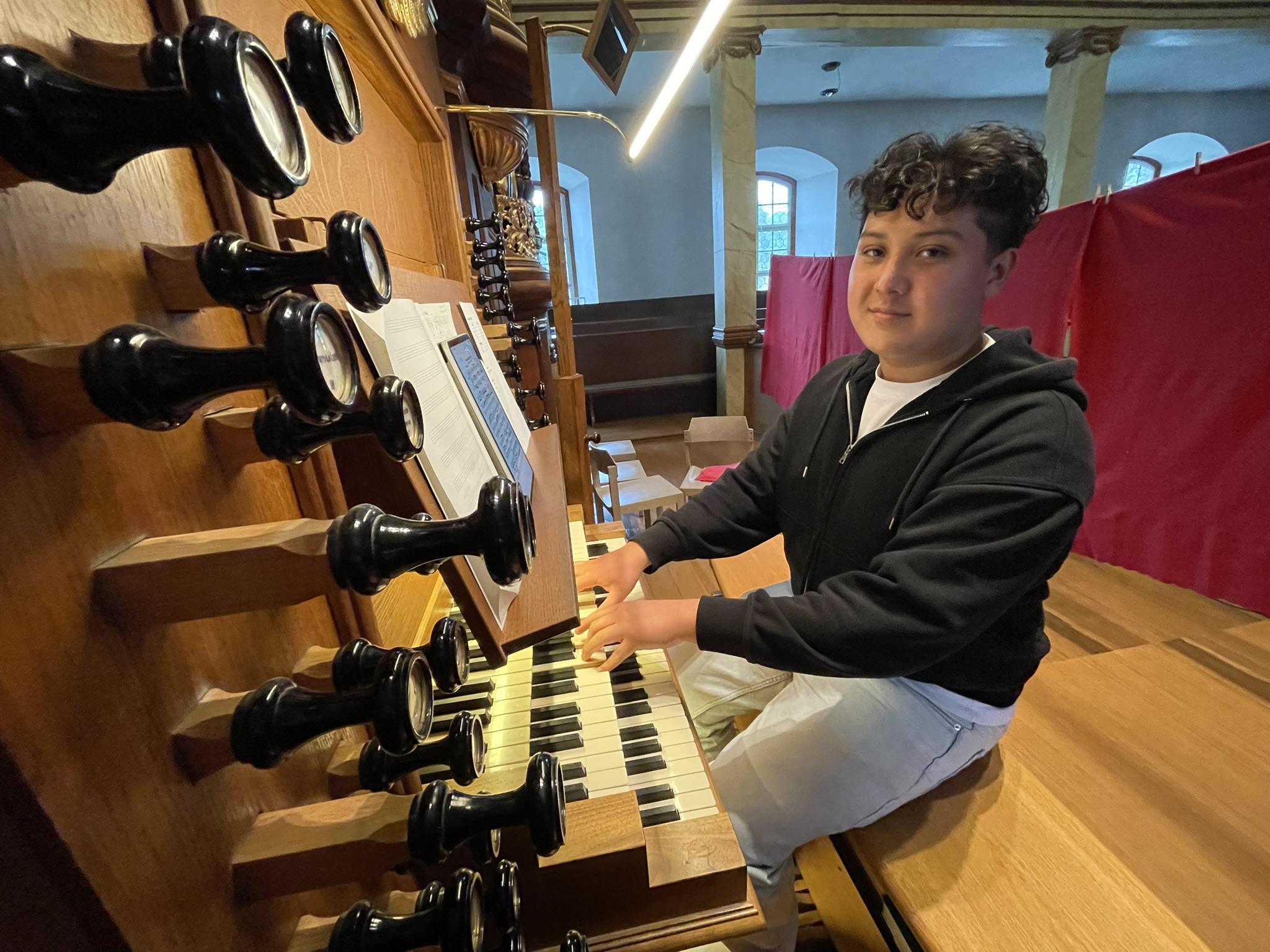 Tyron Unger, Jugendlicher mit dunklen Haaren, trägt einen Pullover, sitzt an der Orgel, die Hände auf den Tasten, den Blick zum Fotografen gerichtet.
