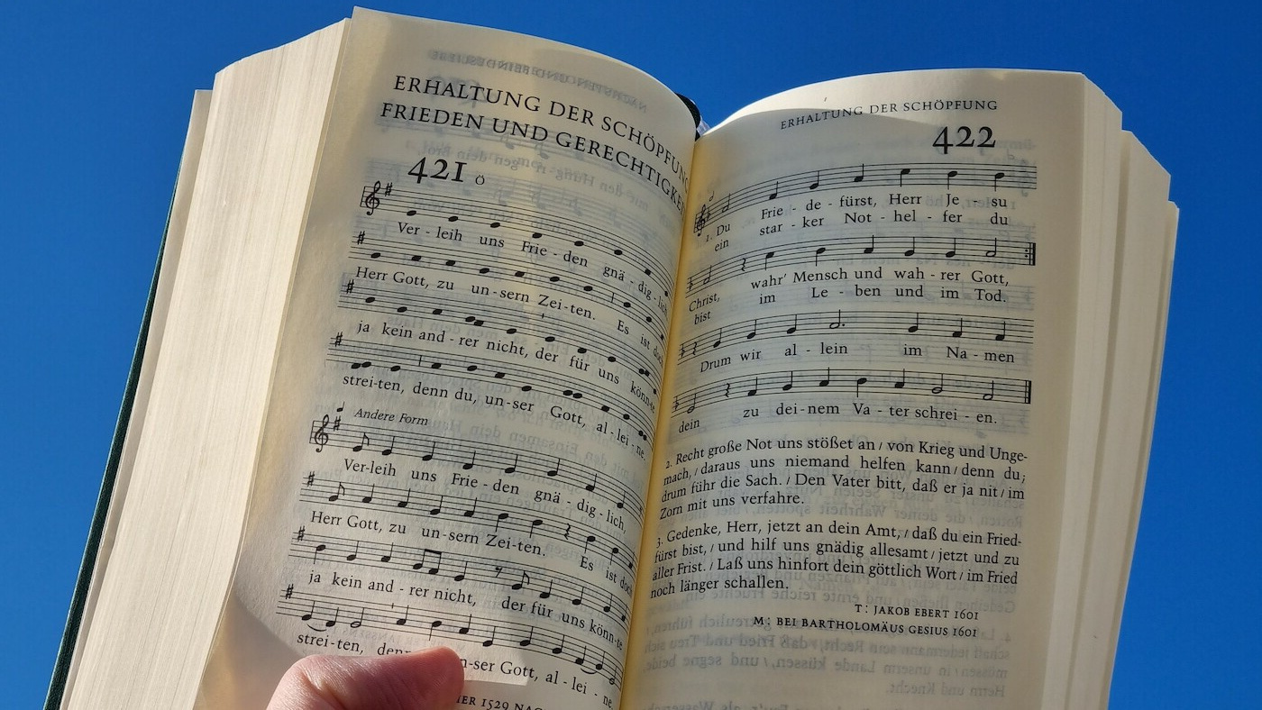 Man blickt auf die Doppelseite im Gesangbuch gegen einen blauen Himmel