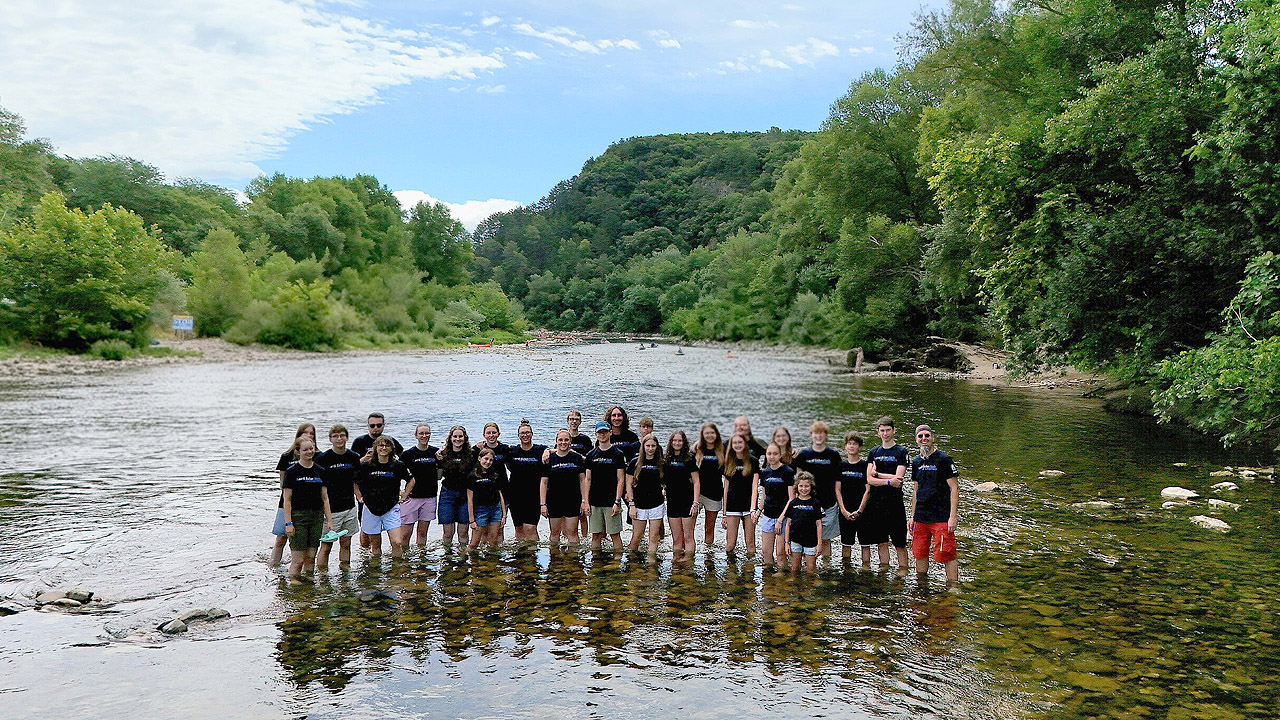 Jugendgruppe, die im flachen Wasser eines Flusses steht, dahinter Berge