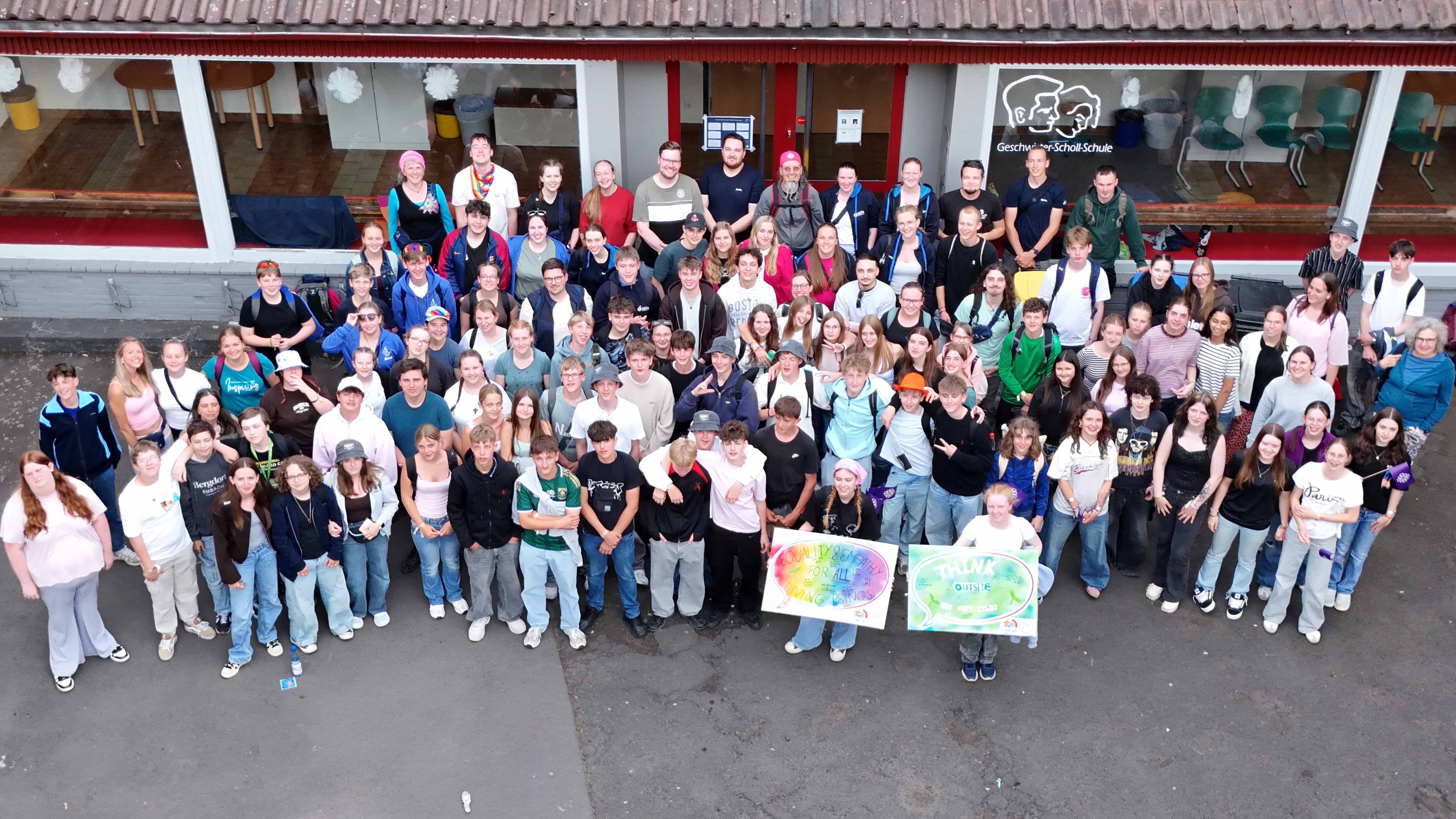 JKT_2026_Gruppenbild_C_Evang_Dekanat_Bergstraße_16zu9.jpg Große Gruppe von Jugendlichen und Erwachsenen vor einem Schulgebäude; einige halten Plakate mit Botschaften zu Vielfalt, Gleichberechtigung und offenem Denken.