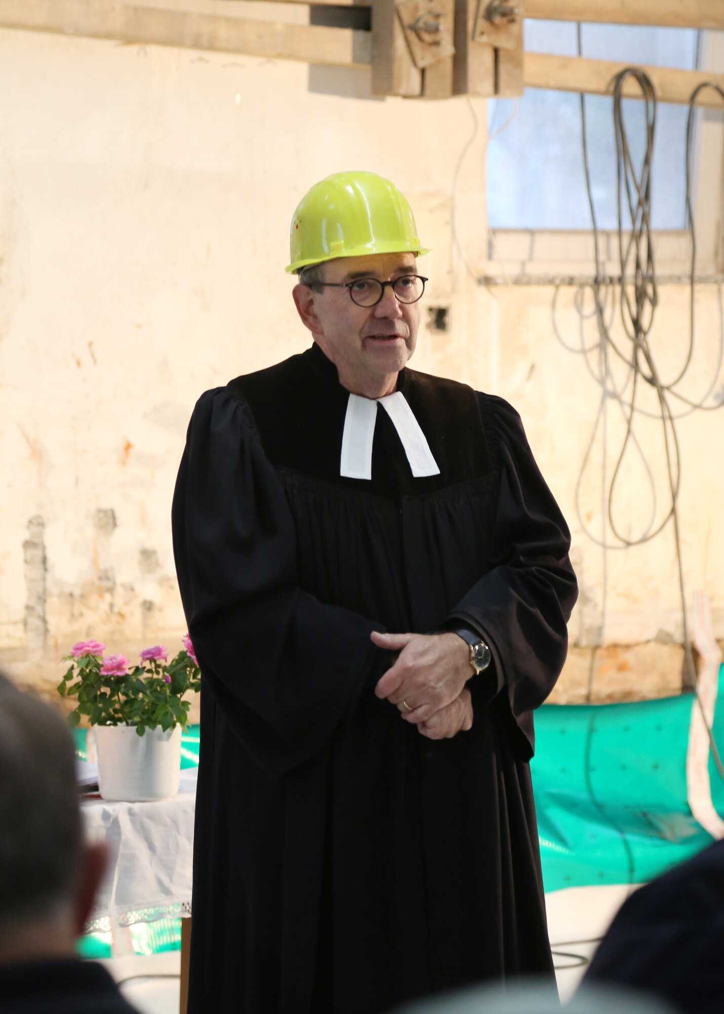 Pfarrer in schwarzem Talar und Beffchen mit gelbem Bauhelm