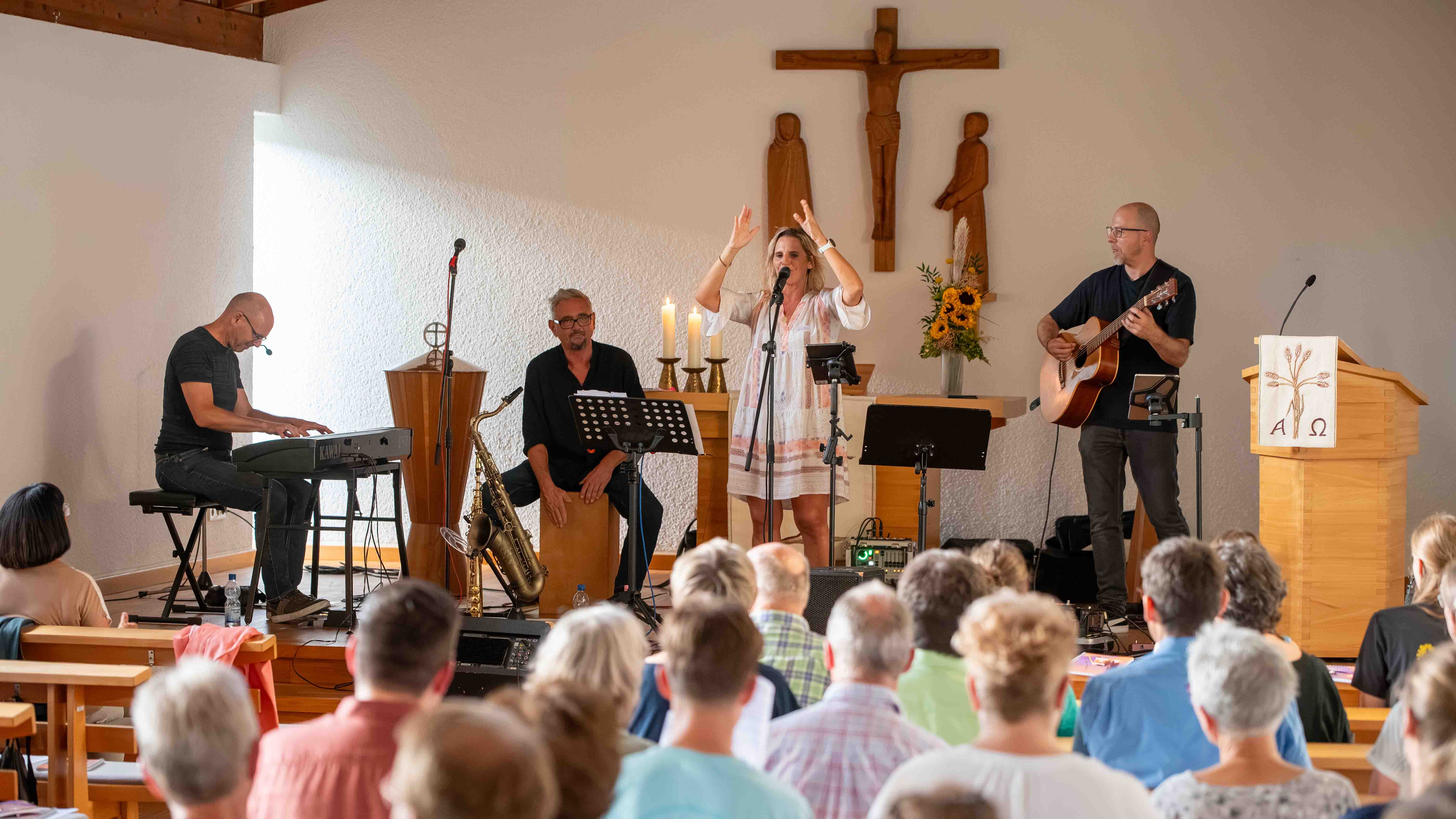 Musikgruppe mit Sängerin, Keyboarder, Saxofonist und Gitarrist tritt vor Publikum in einer Kirche auf.