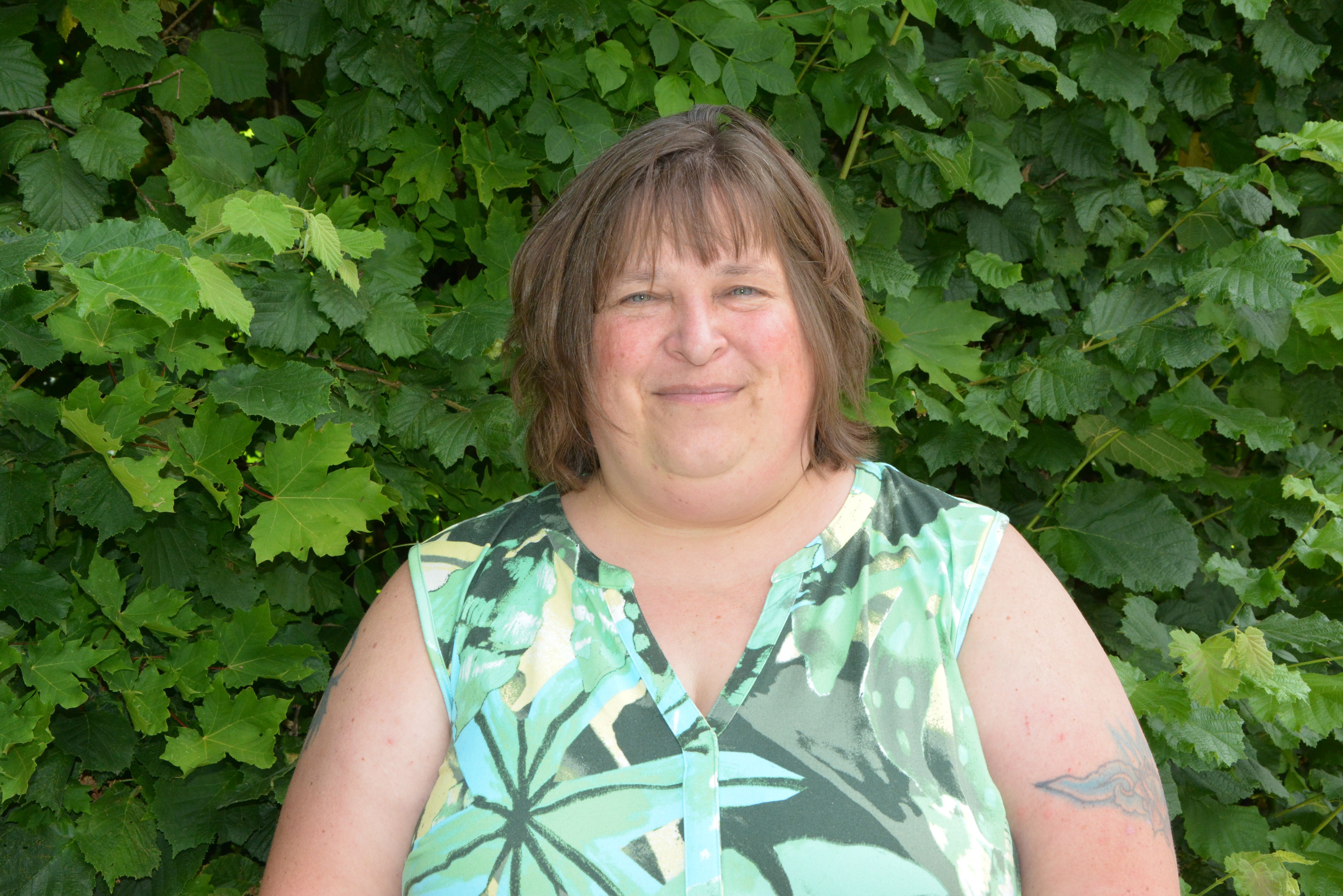 Vorsitzende Petra Szameit im grünen Oberteil vor einer Hecke