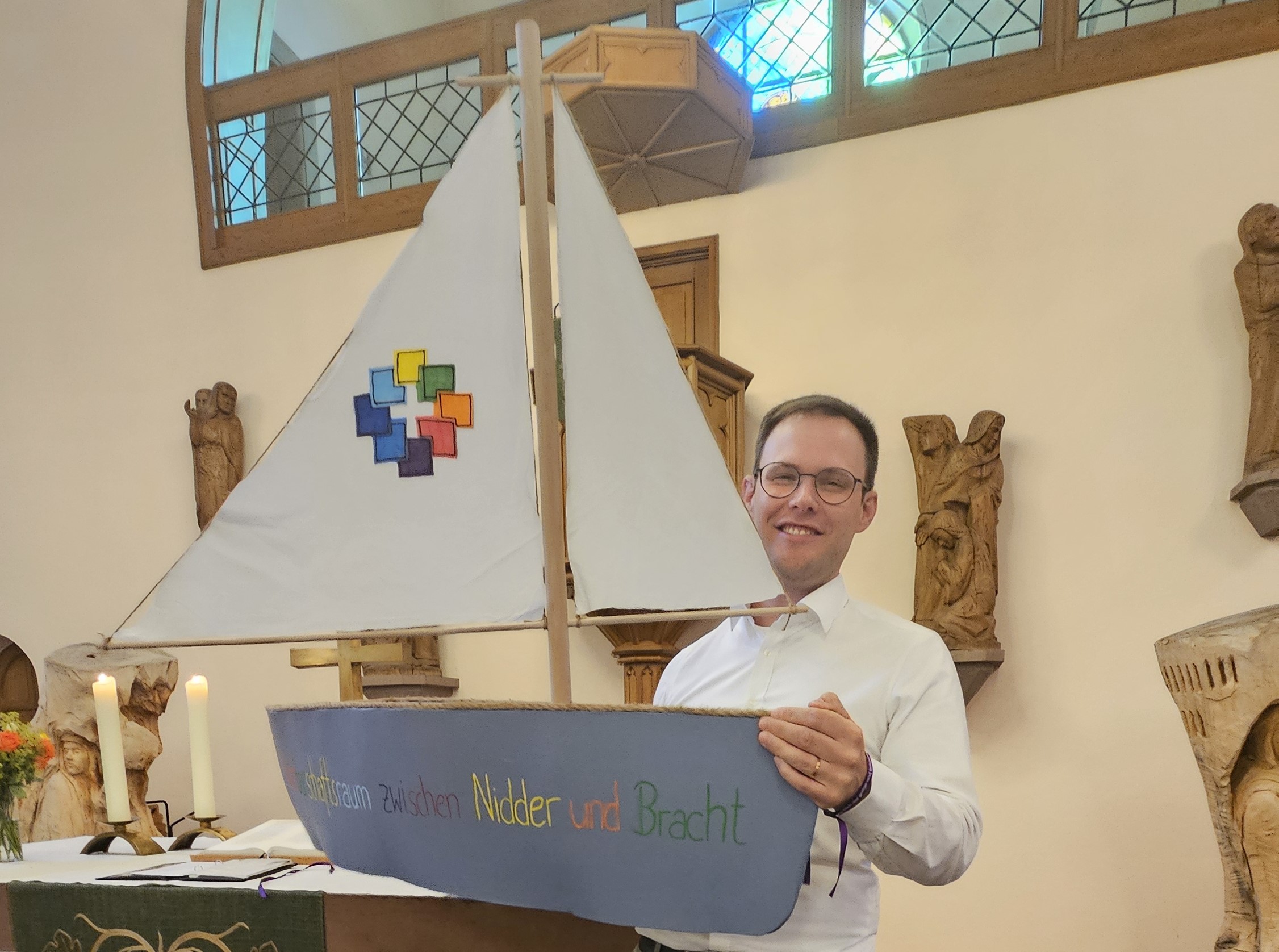 Lektor Jan Röder hält vor dem Altar ein Schiff in die Höhe, das er als Symbol für die gemeinsame Reise im Nachbarschaftsraum gebaut hat.