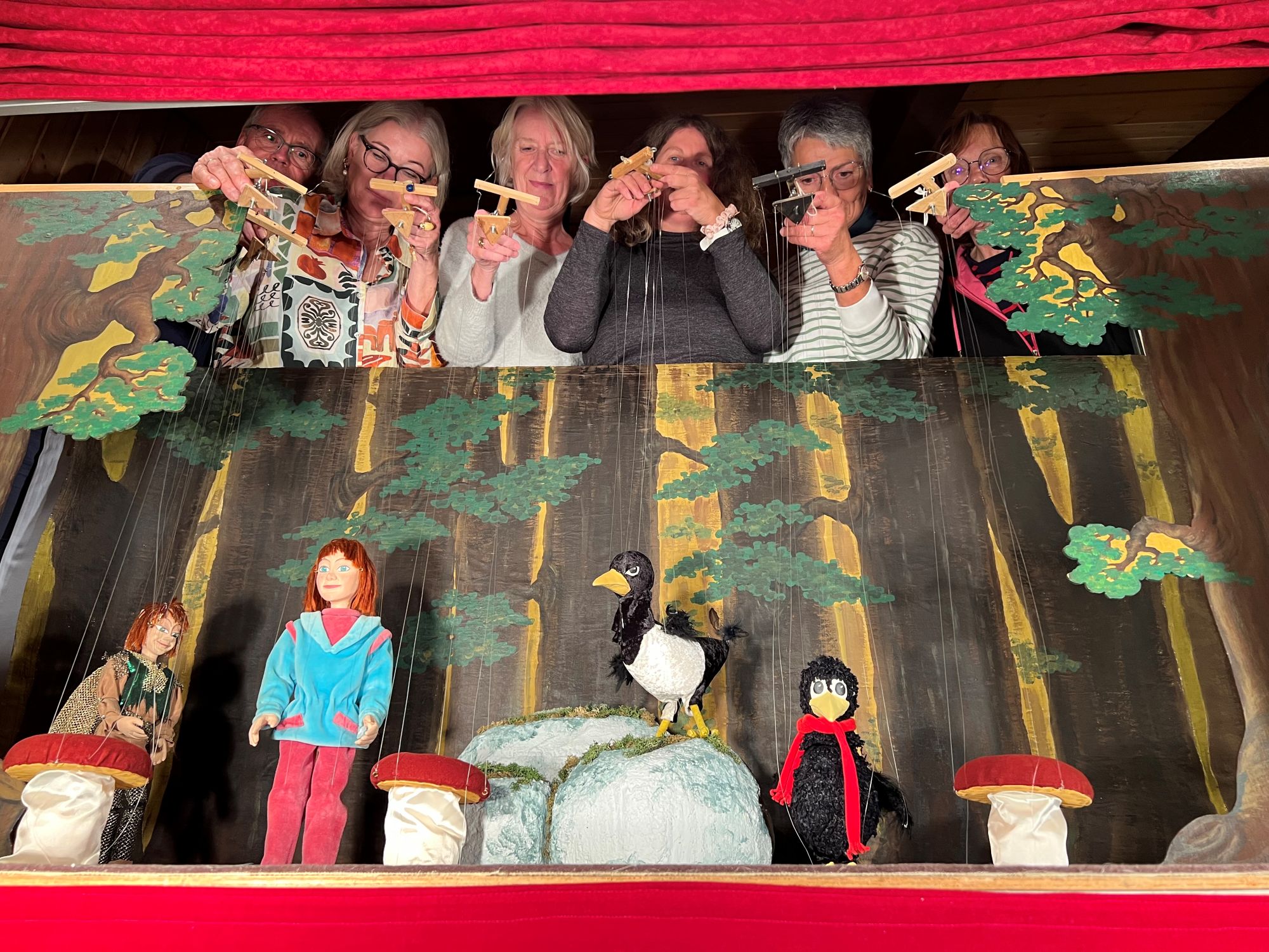 Bringen Pilze zum Tanzen und Raben zum Niesen: (von links) Günter Wilde, Heike Göhler, Brigitte Tönsing, Andrea Schmucker, Gudrun Hartmann und Marion Koch; nicht auf dem Foto ist Doris Funck. Eine Marionettenspielbühne, im oberen Bereich einige Personen, die Marionetten an den Fäden führen.