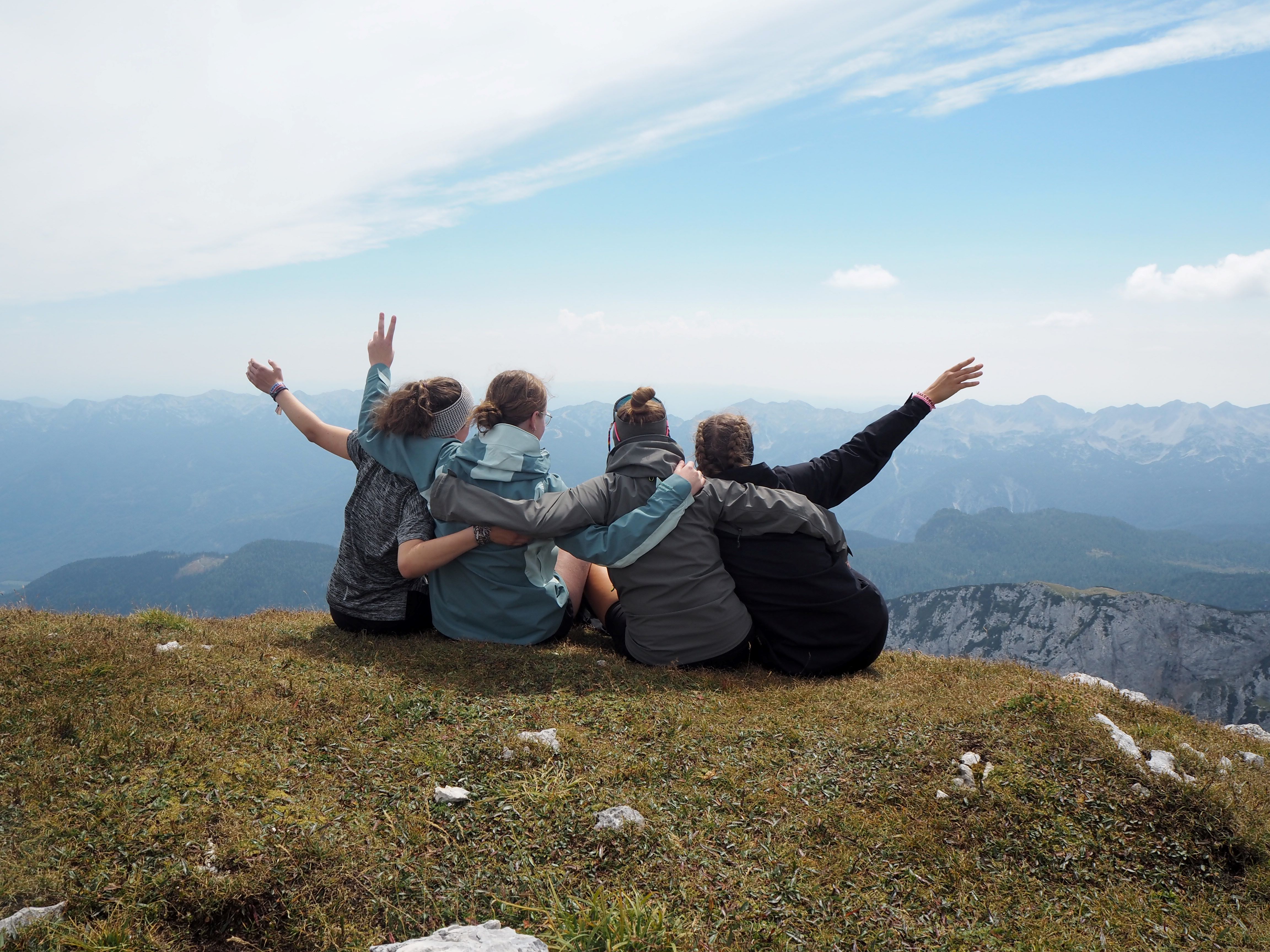 Jugendliche einer Dekanatsfreizeit sitzen mit dem Rücken zur Kamera auf einem Berggipfel in Slowenien