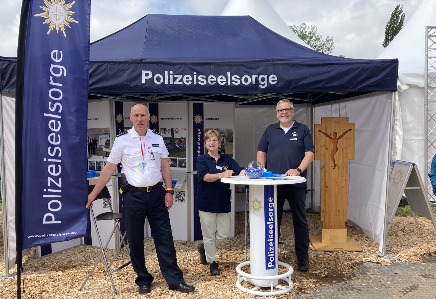 Vor einem Zelt stehen ein Polizist und zwei Polizeiseelsorger