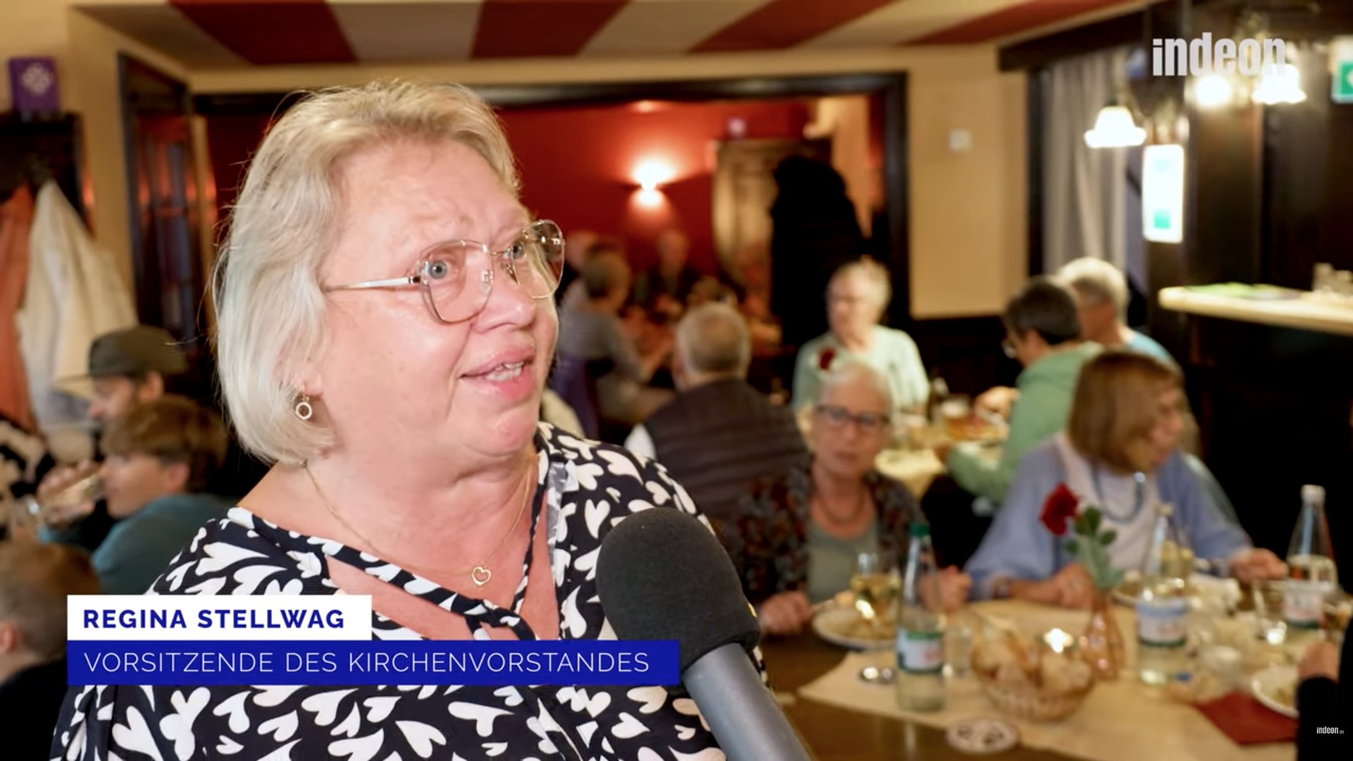 Eine Frau spricht in einer Mikrofon, sie wird interviewt. Im Hintergrund sitzen viele Menschen in einem Gastraum.