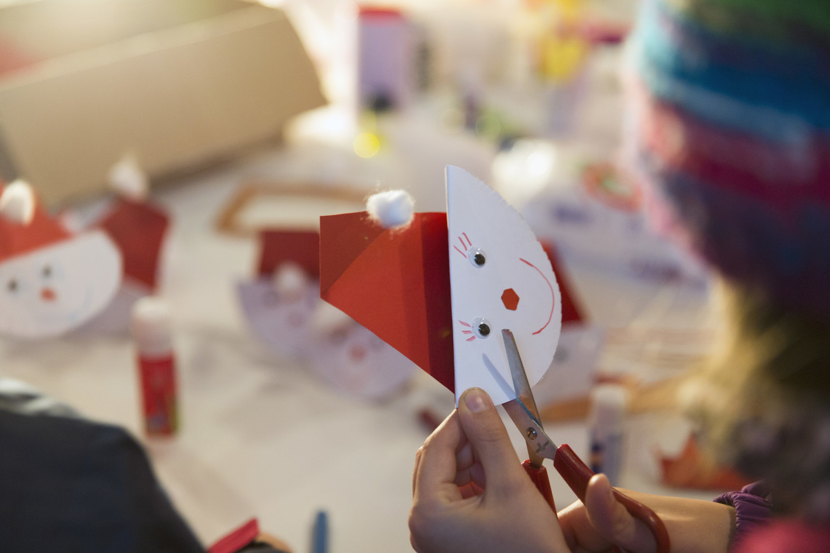 Kind schneidet mit Schere einen Weihnachtsmann aus.