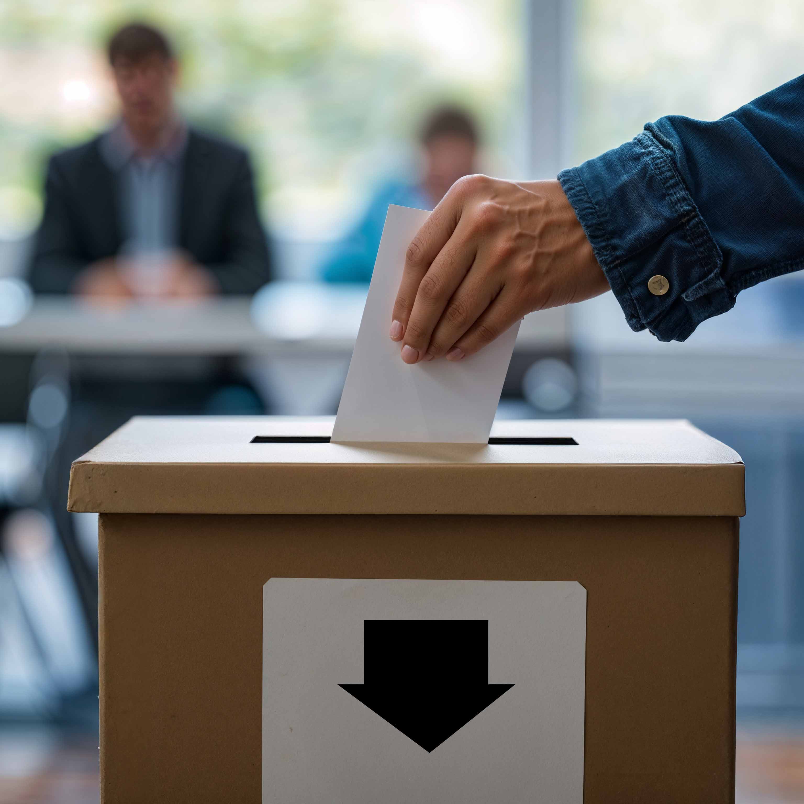 Hand wirft Stimmzettel in Wahlurne