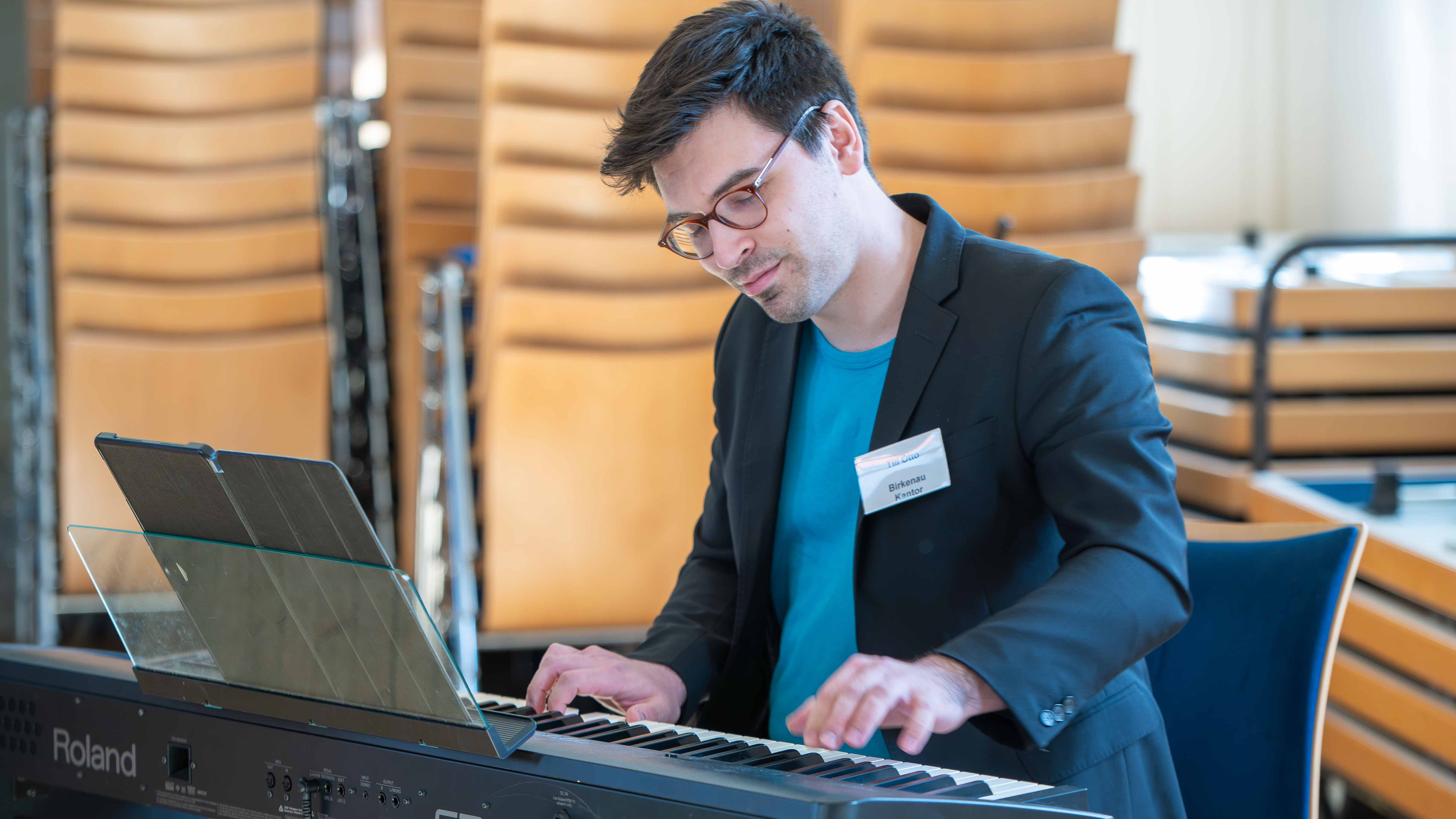 Alternativtext:  Mann mit Brille spielt konzentriert auf einem elektronischen Keyboard in einem Veranstaltungsraum. 