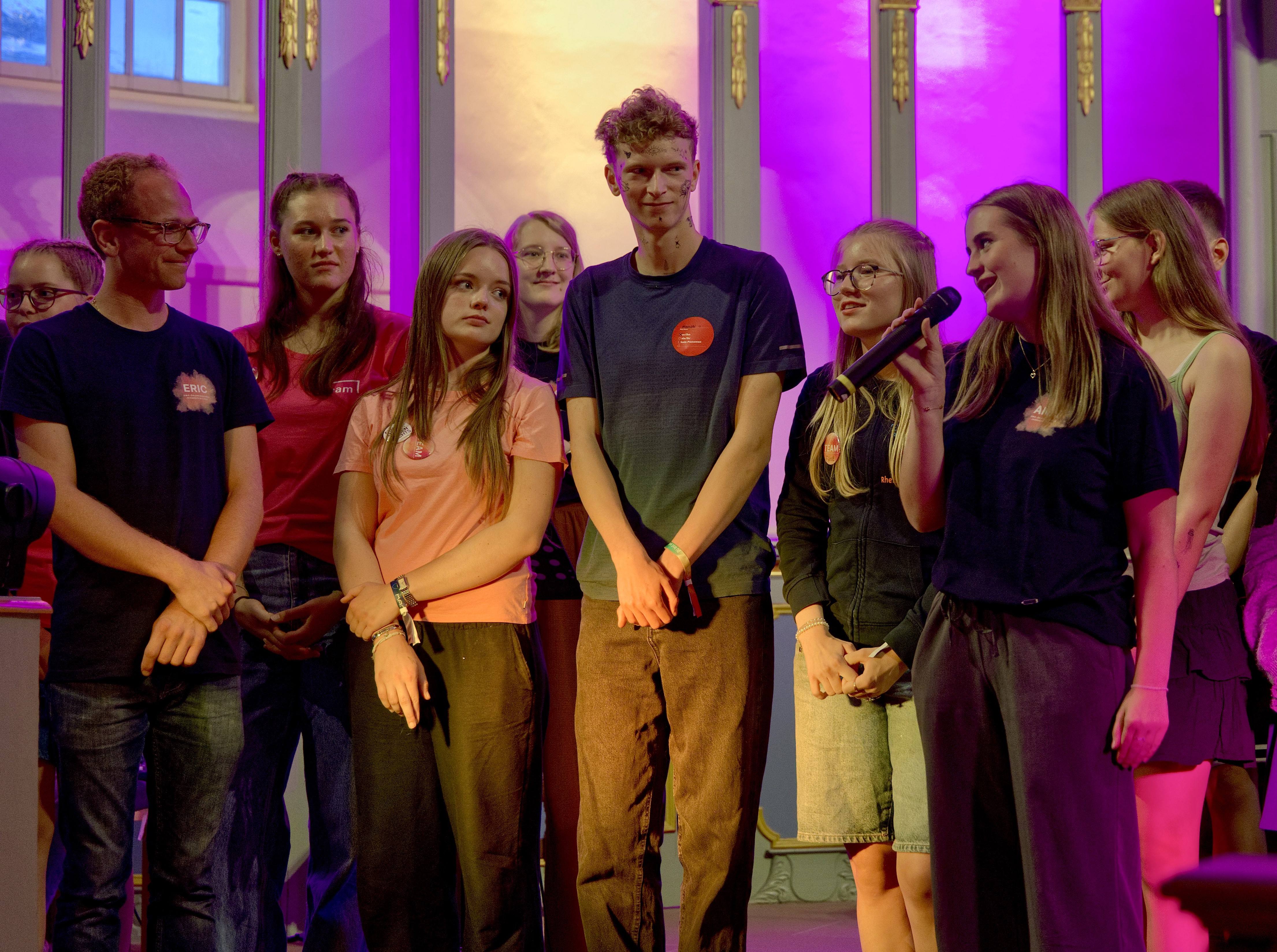 Annika moderiert beim Abschlussgottesdienst von OMG im Kreise mit anderen Jugendliche. Sie stehen im violett beleuchtete Altarraum. 