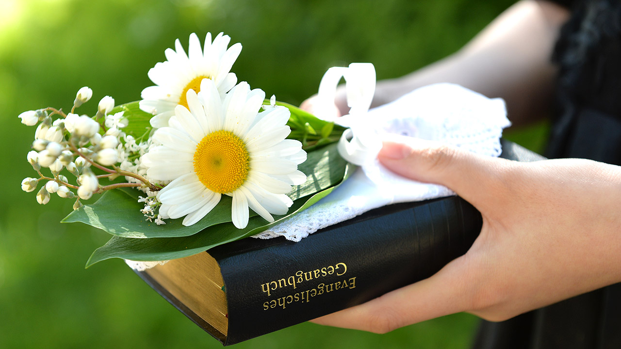 Hand, die einen Blumenstrauß und ein Gesangbuch hält
