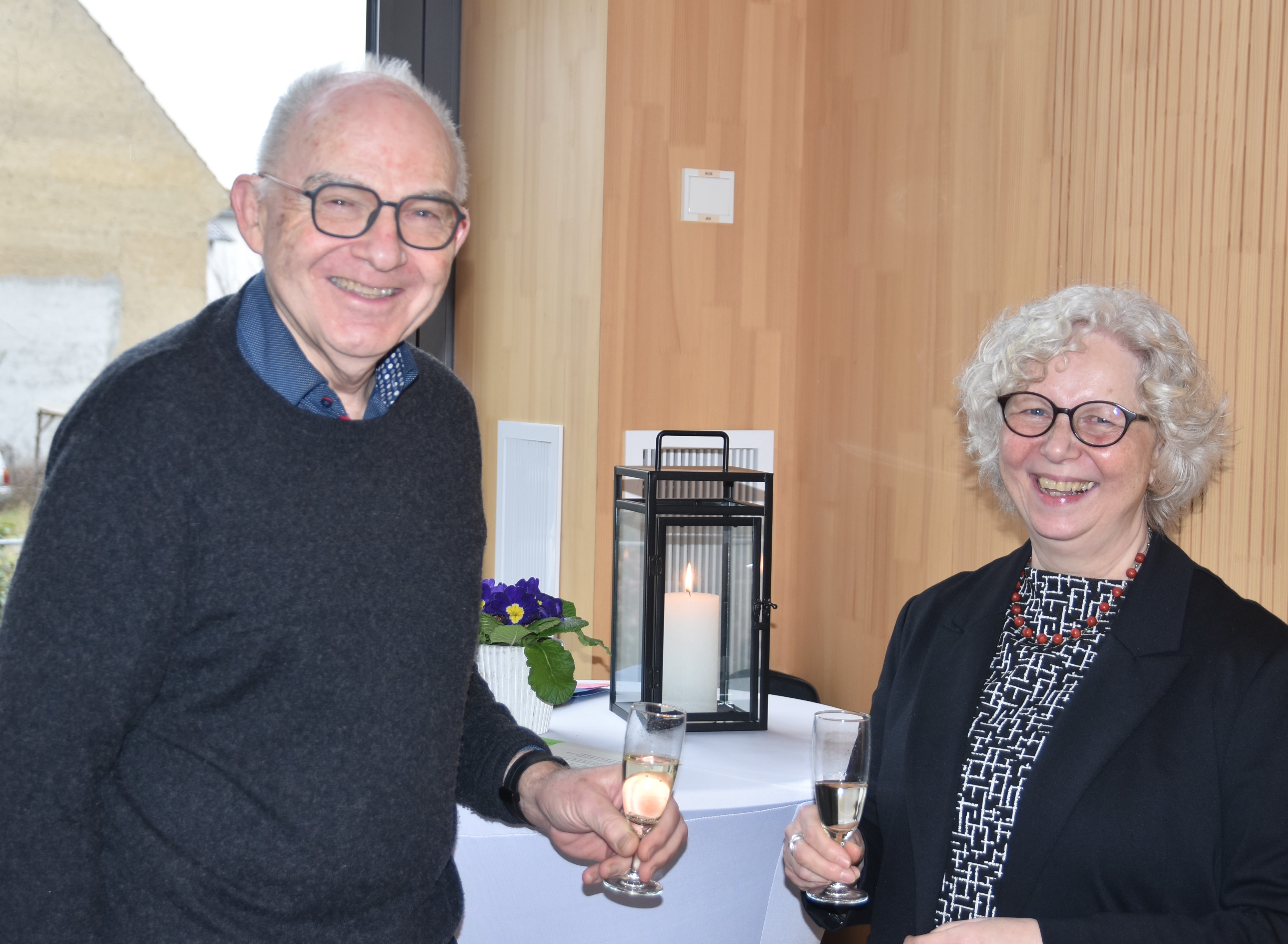 Rolf Hartmann und Rita Stoll stehen im Johannitersaal des Dekanats und stoßen mit Sekt an.