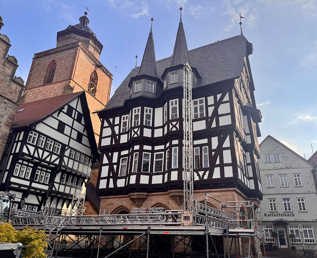Historisches Fachwerk-Rathaus mit hohen Giebeln und Türmen, davor ein Gerüstaufbau auf einem Marktplatz.