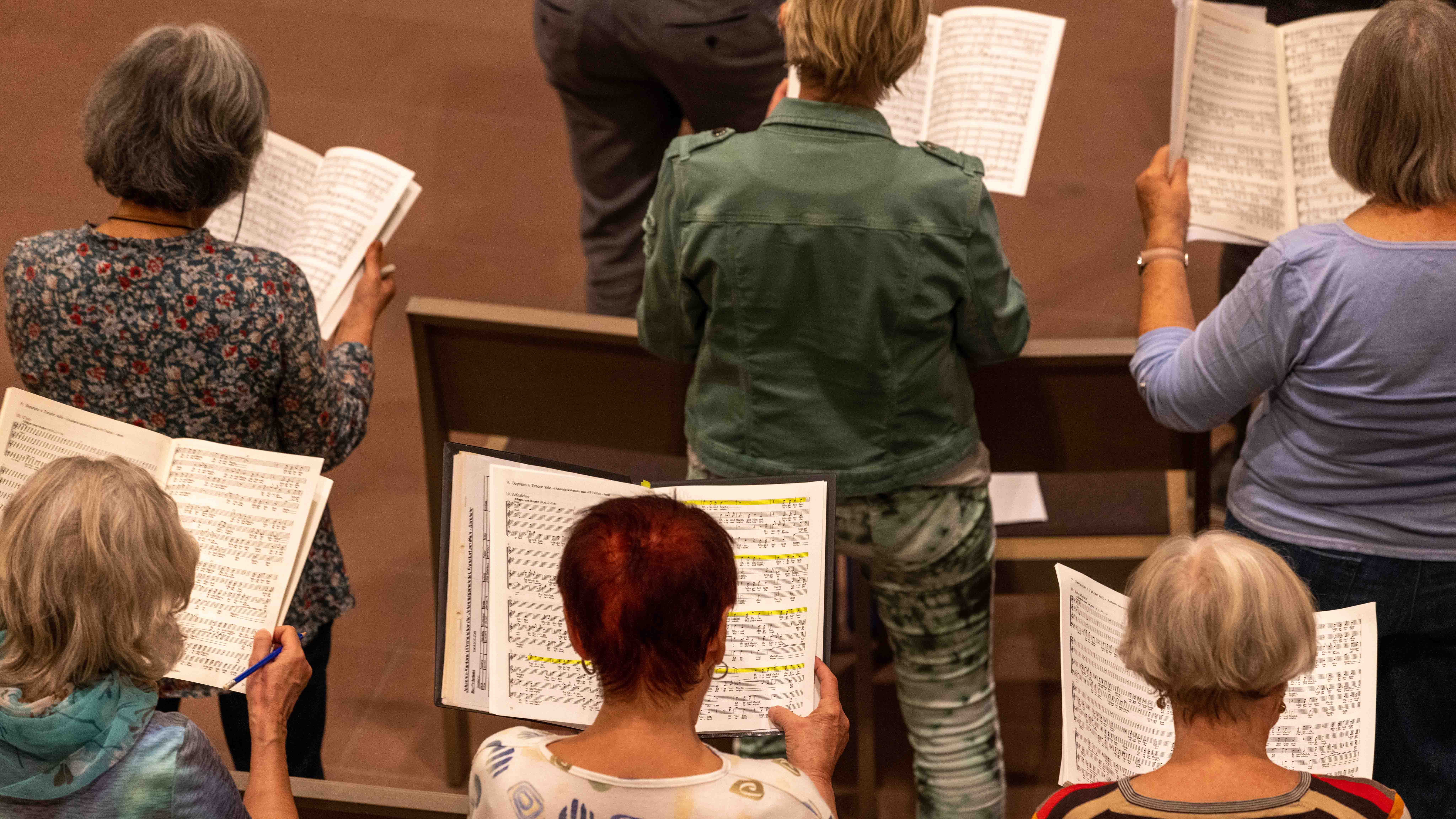 Mehrere Personen stehen mit geöffneten Notenblättern in einem Chor und singen gemeinsam.