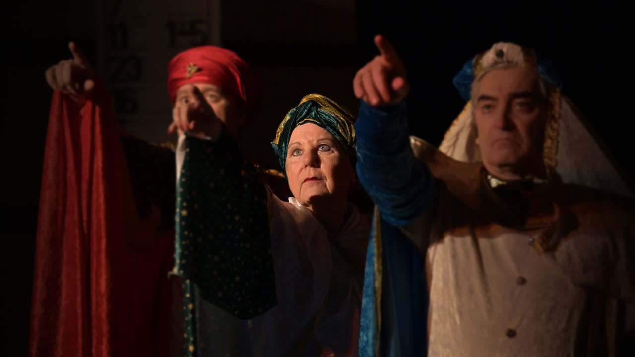 Cherubs_Theater_Herodias_C_Peter_Hahn_16zu9.jpg Drei Personen in historischen Theaterkostümen stehen auf einer dunkel beleuchteten Bühne. Im Mittelpunkt blickt eine Frau mit blau-goldenem Turban und ernstem Gesichtsausdruck nach vorne. Die beiden Personen neben ihr tragen auffällige Kopfbedeckungen und zeigen mit ausgestreckten Armen und erhobenen Zeigefingern in Richtung Publikum. Die Szene stammt aus der Theaterproduktion „Herodias oder über die (Un-)Erträglichkeit von Belehrung und Moral“ des Cherubs-Theaters.
