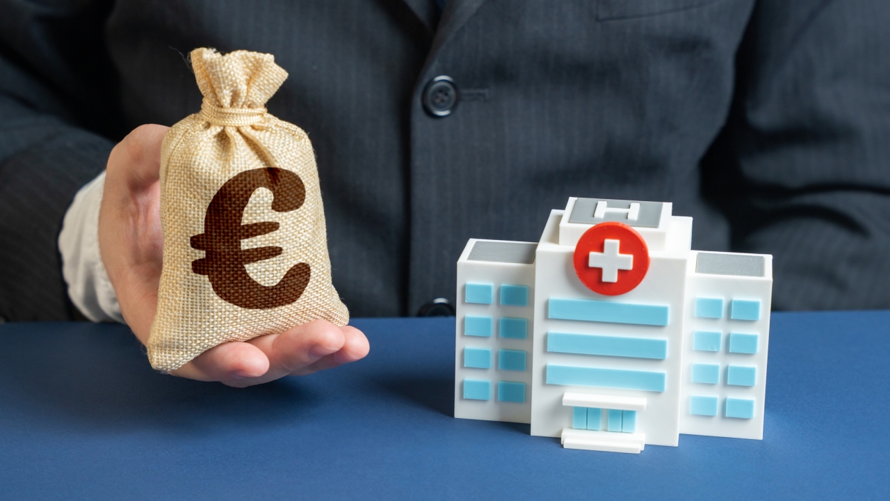 Spenden Krankenhaus Modell eines Krankenhauses und Mann mit kleinem Geldsack, auf dem ein Euro-Zeichen ist