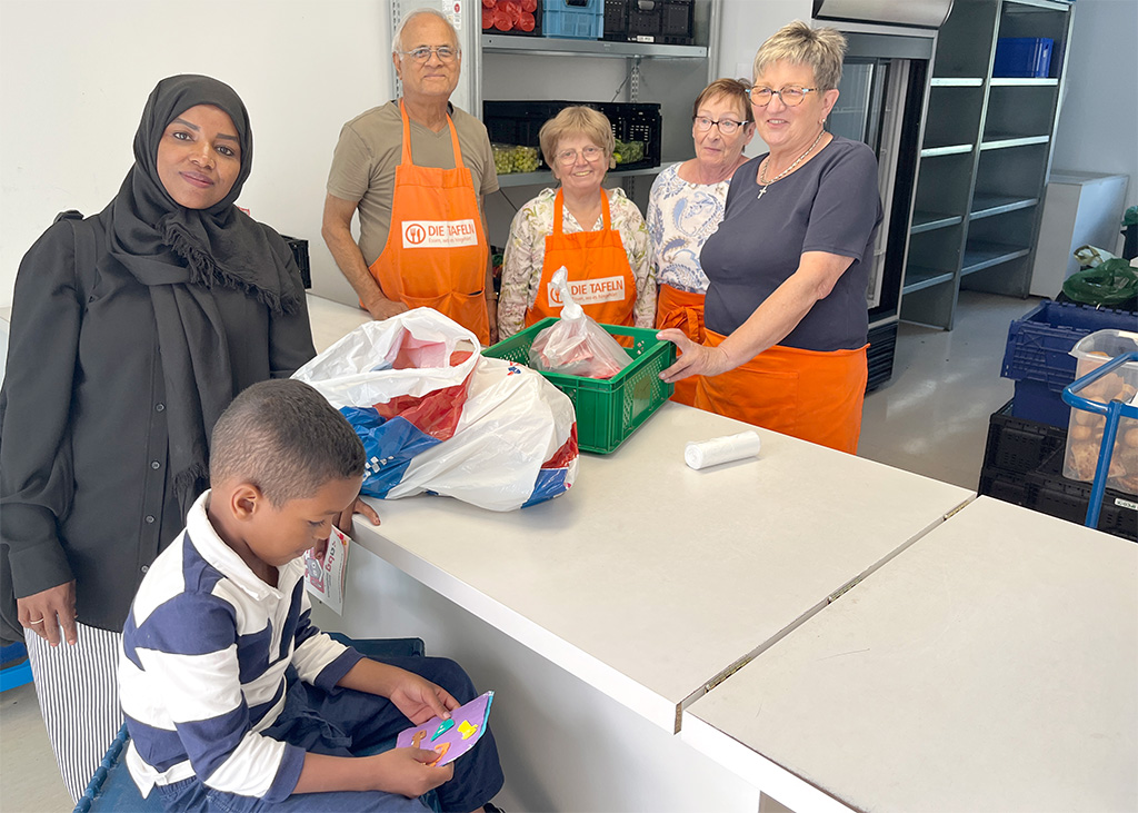 Tafel 2025 Menschen schauen in die Kamera. Sie stehen um einen Thresen herum. Im Hintergrund sind Lebensmittel zu sehen.