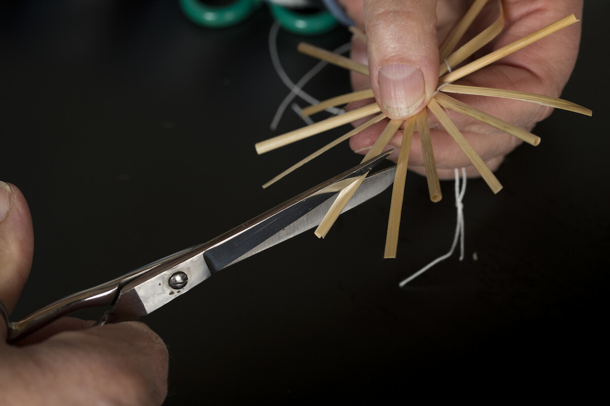 Strohsterne basteln Eine Person schneidet mir einer Schere einen Strohstern zu. Die einzelnen "Strahlen" werden auf eine einheitliche Länge geschnitten.