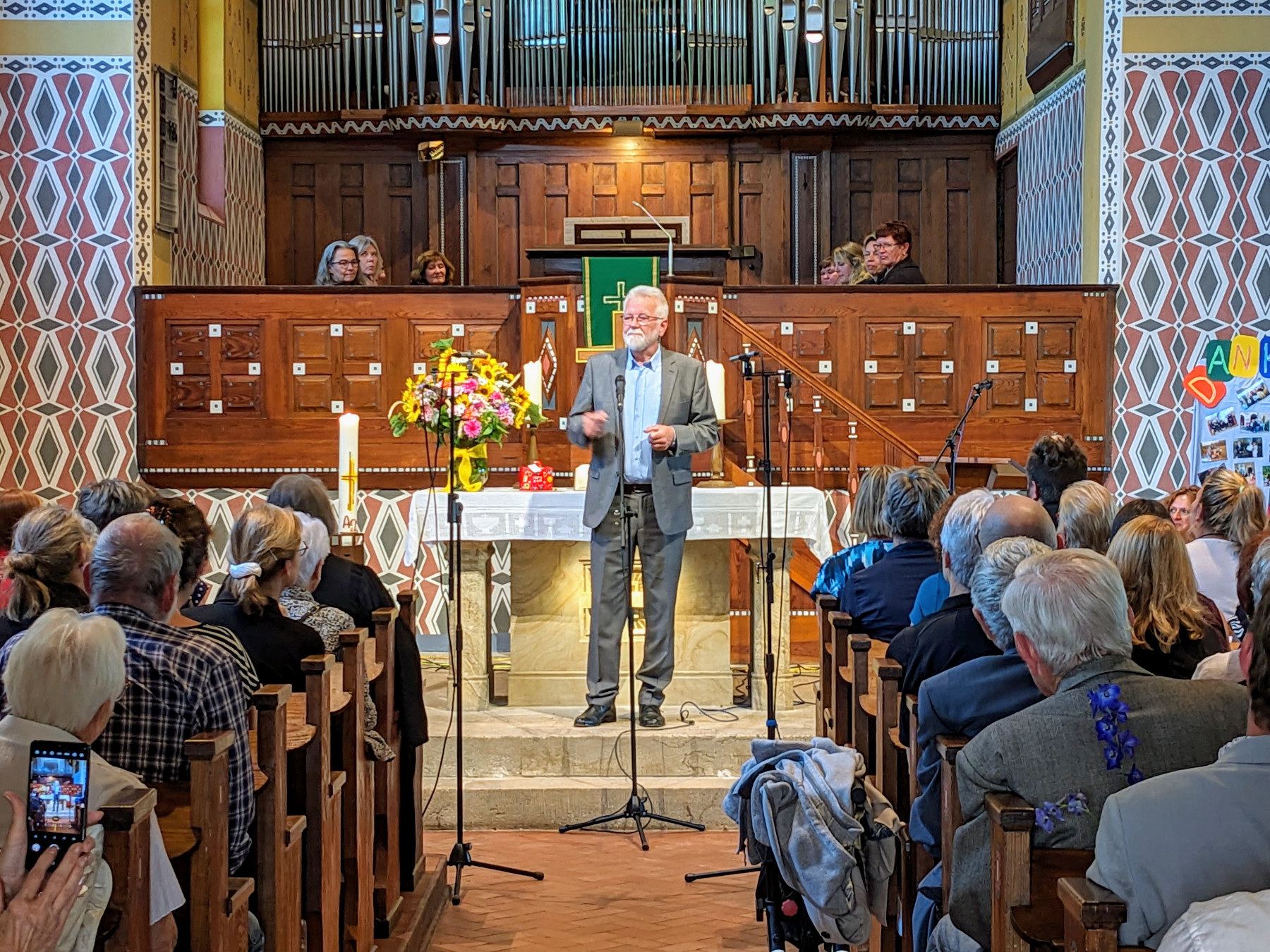 Blick in eine voll besetzte Kirche. Vor dem Altar steht ein Mann im grauen Anzug, der zur Gemeinde blickt.