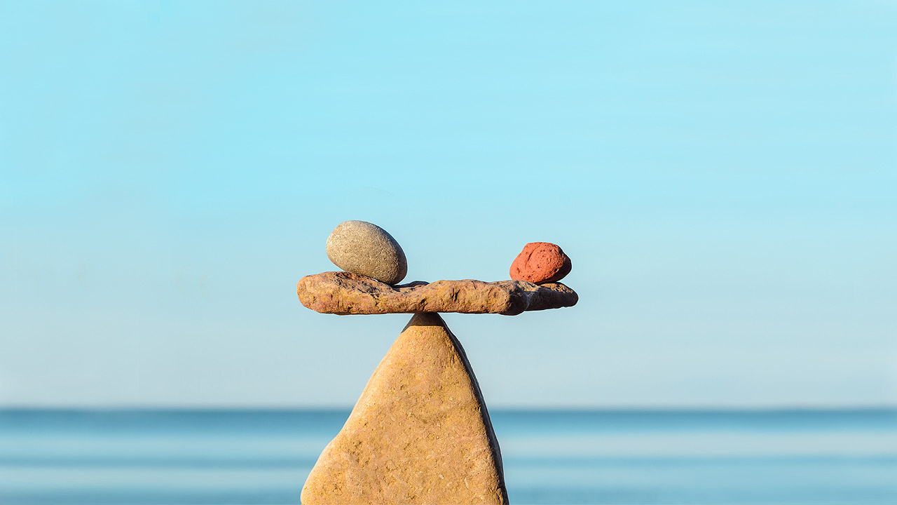 Klimafasten - Balance Steinmännchen am Meer in Form einer Waage, auf dem Querstein liegen links und rechts zwei kleiner Steine