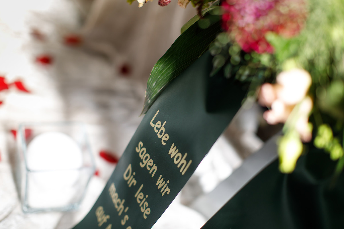Bestattung Trauerfeier Begräbnis Urne Friedhof 13 Ein schwarzes Band mit Text am Kranz auf dem Grab