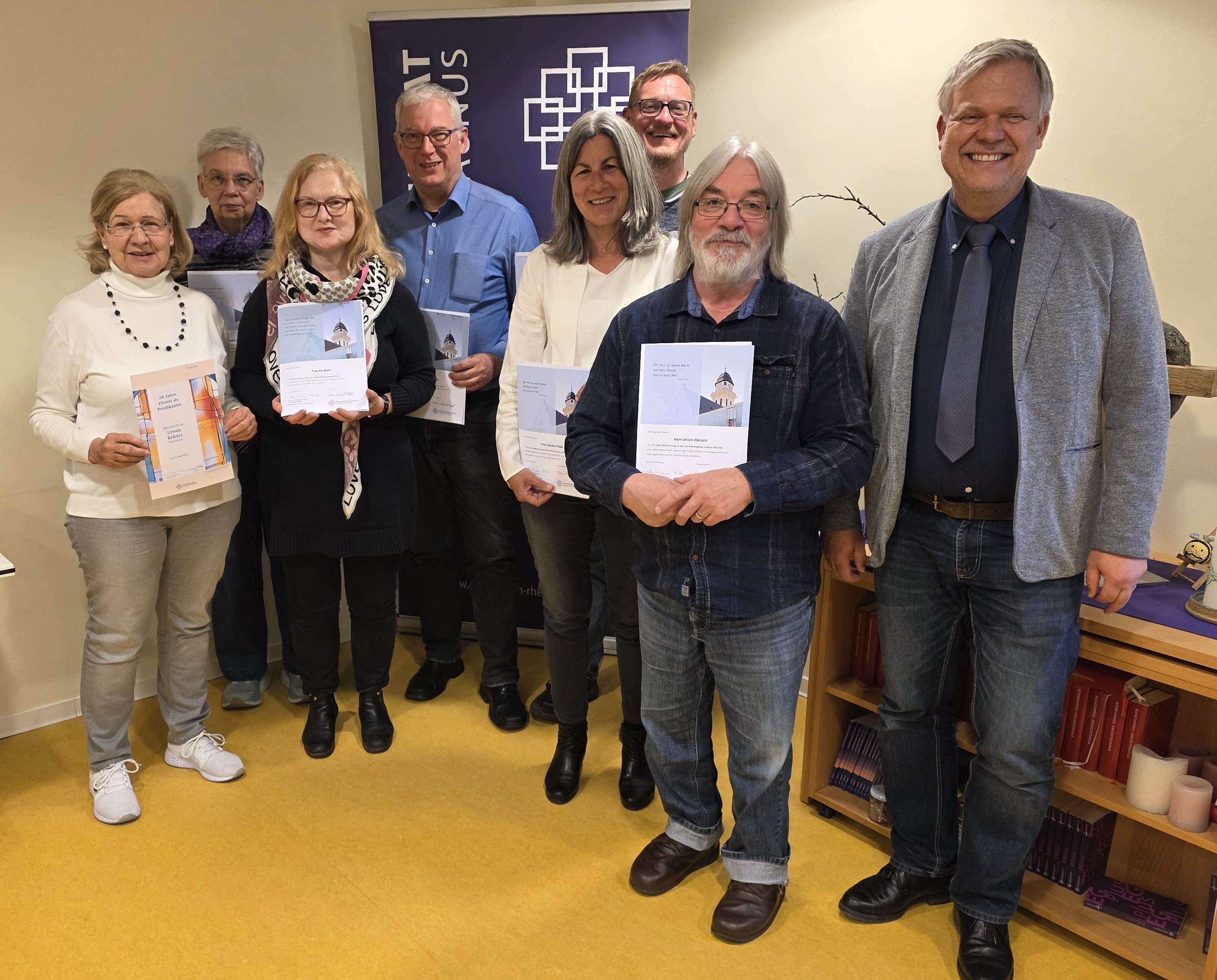 Eine Gruppe von Menschen steht lächelnd vor einem lila Aufsteller. Sie halten Urkunden in ihrem Händen.