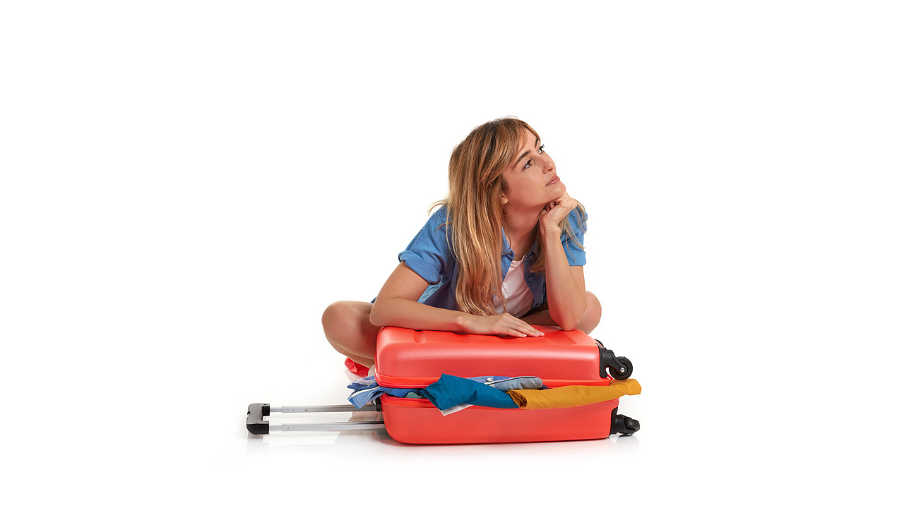 Eine Frau sitzt nachdenklich hinter ihrem noch nicht fertig gepackten Koffer