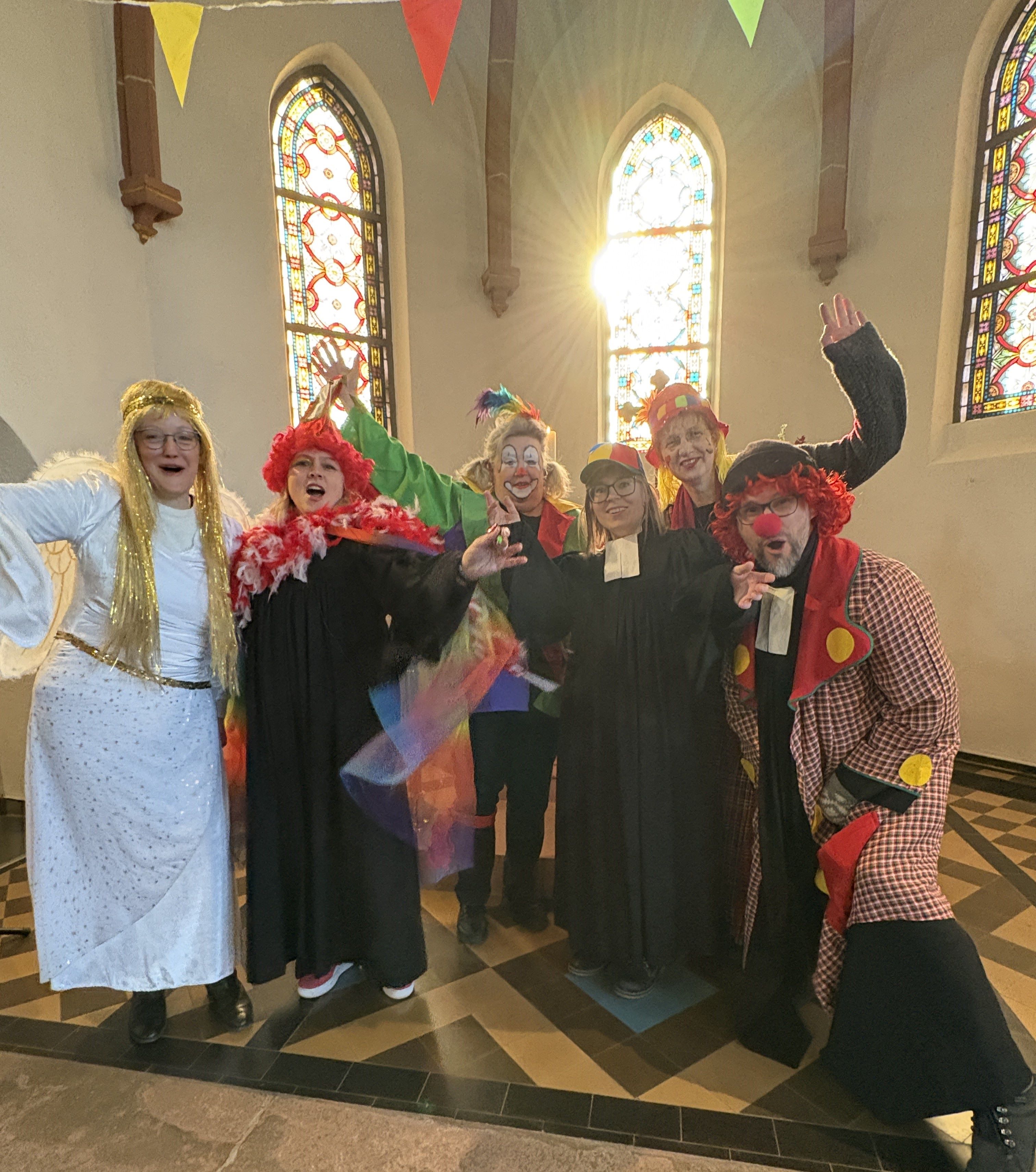 Sechs Menschen als Engel und Clowns verkleidet stehen im Altarram und winken fröhlich in die Kamera
