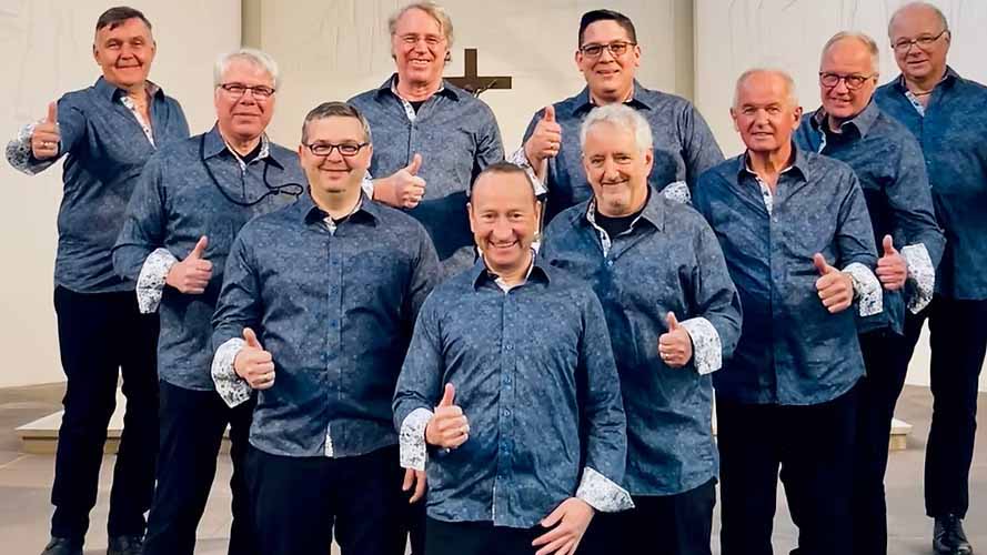 Zehn Männer in einheitlichen blauen Hemden stehen in drei Reihen vor einem Kreuz und zeigen lächelnd den Daumen nach oben.