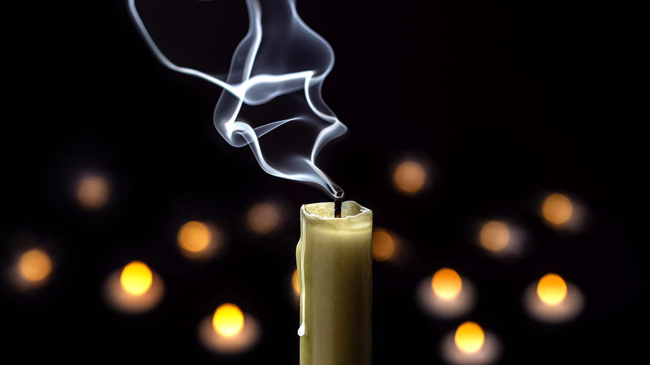 Vorne eine erloschene Kerze, im Hintergrund Lichter