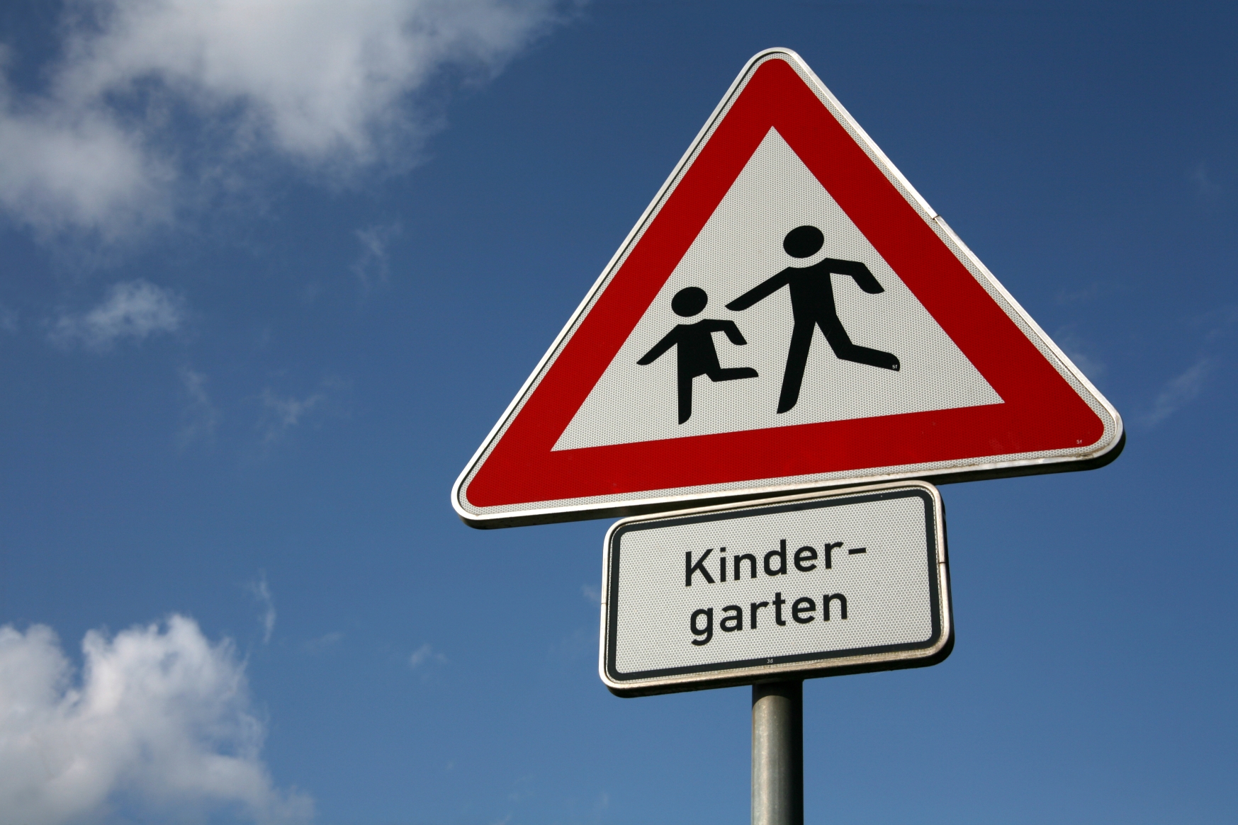 Verkehrsschild "Spielende Kinder" mit Unterschild "Kindergarten" vor einem blauen Himmel